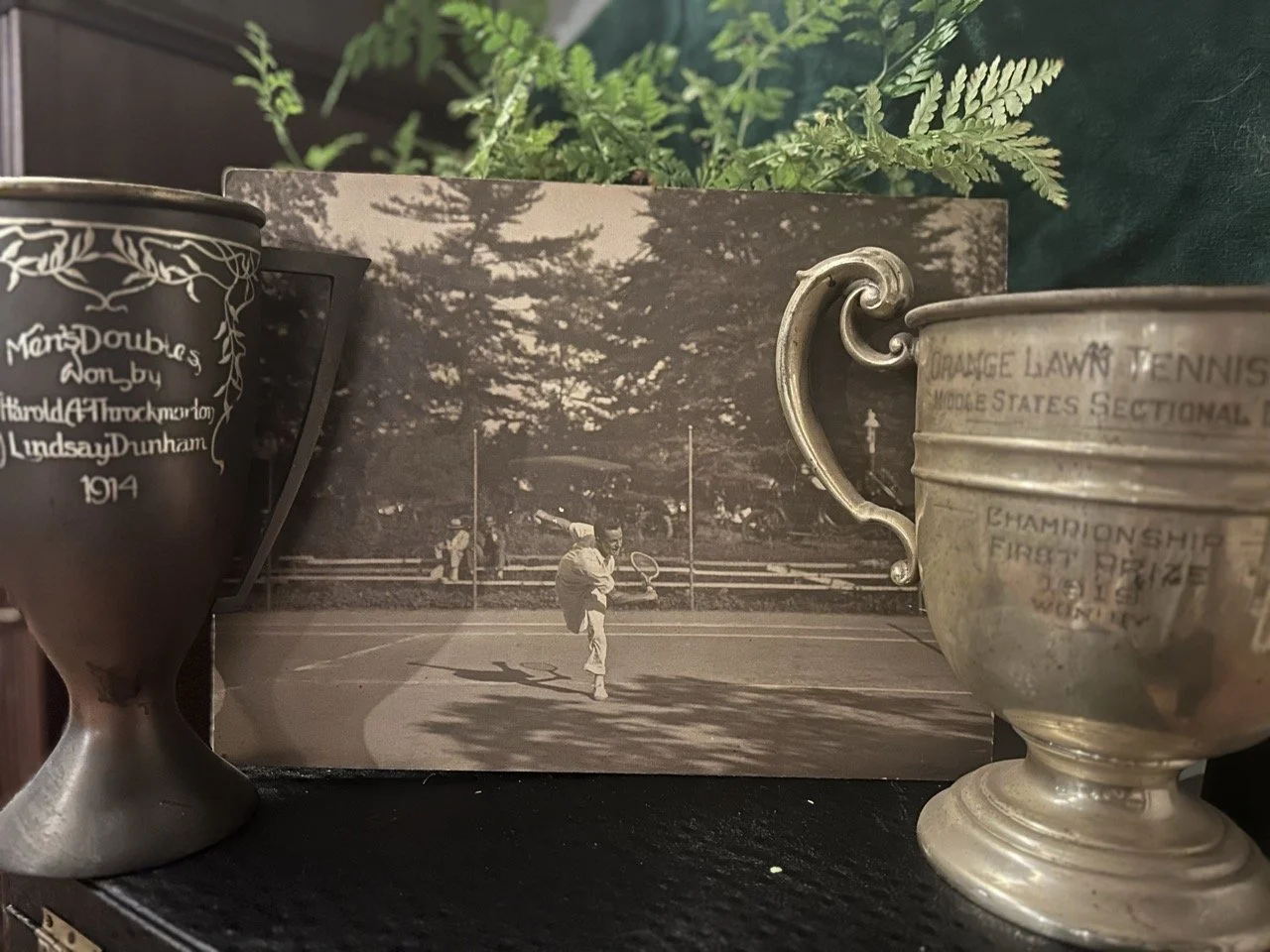 A black and white photograph of Shelly's grandfather competing, with two of his tennis trophies surrounding the photo.