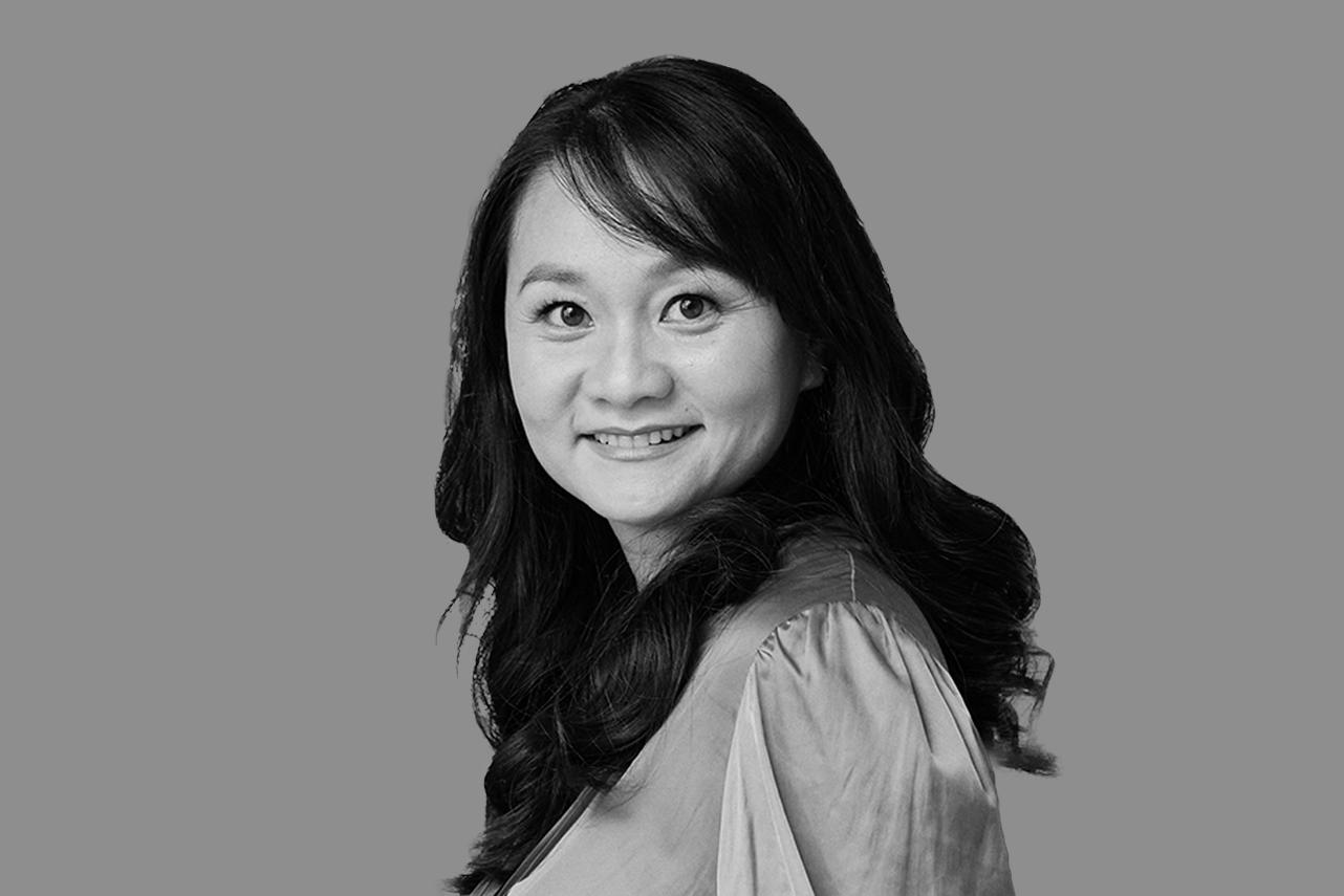 Black and white portrait of a woman with long wavy hair, smiling, against a plain background.