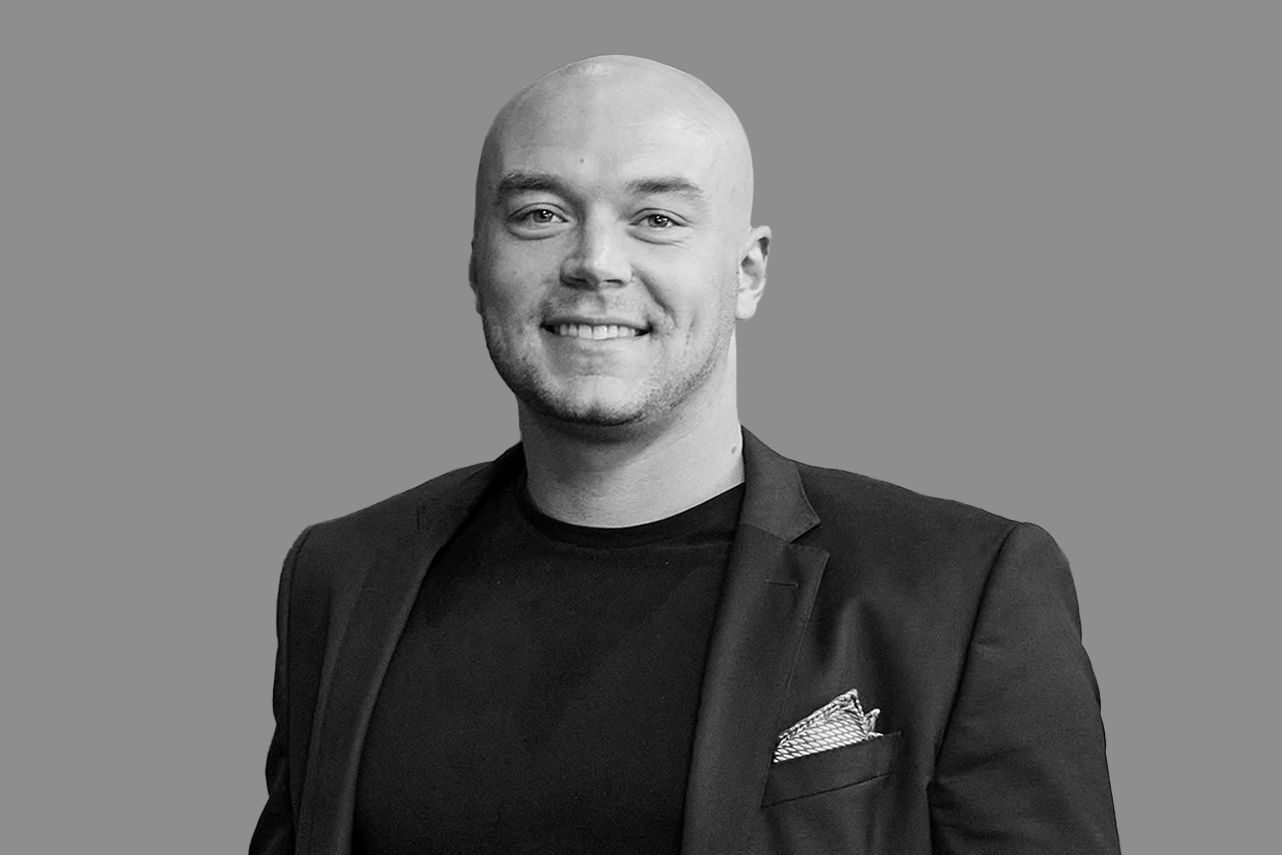 Black and white portrait of a smiling man in a suit with a pocket square, against a plain background.