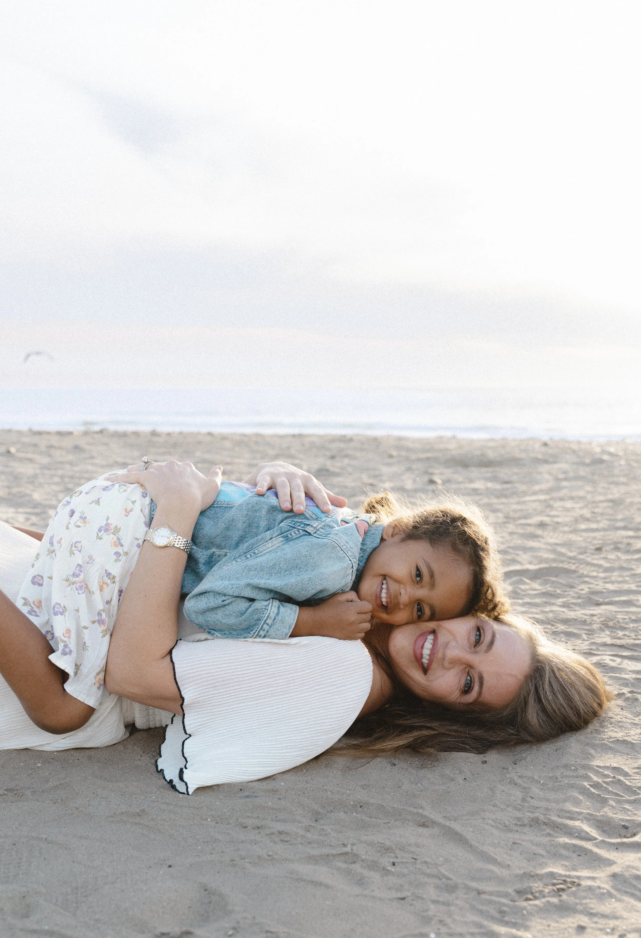 Mother and daughter laughing together at Ponto Beach in Carlsbad, California during a coastal family photography session by the Salt and Serenity.