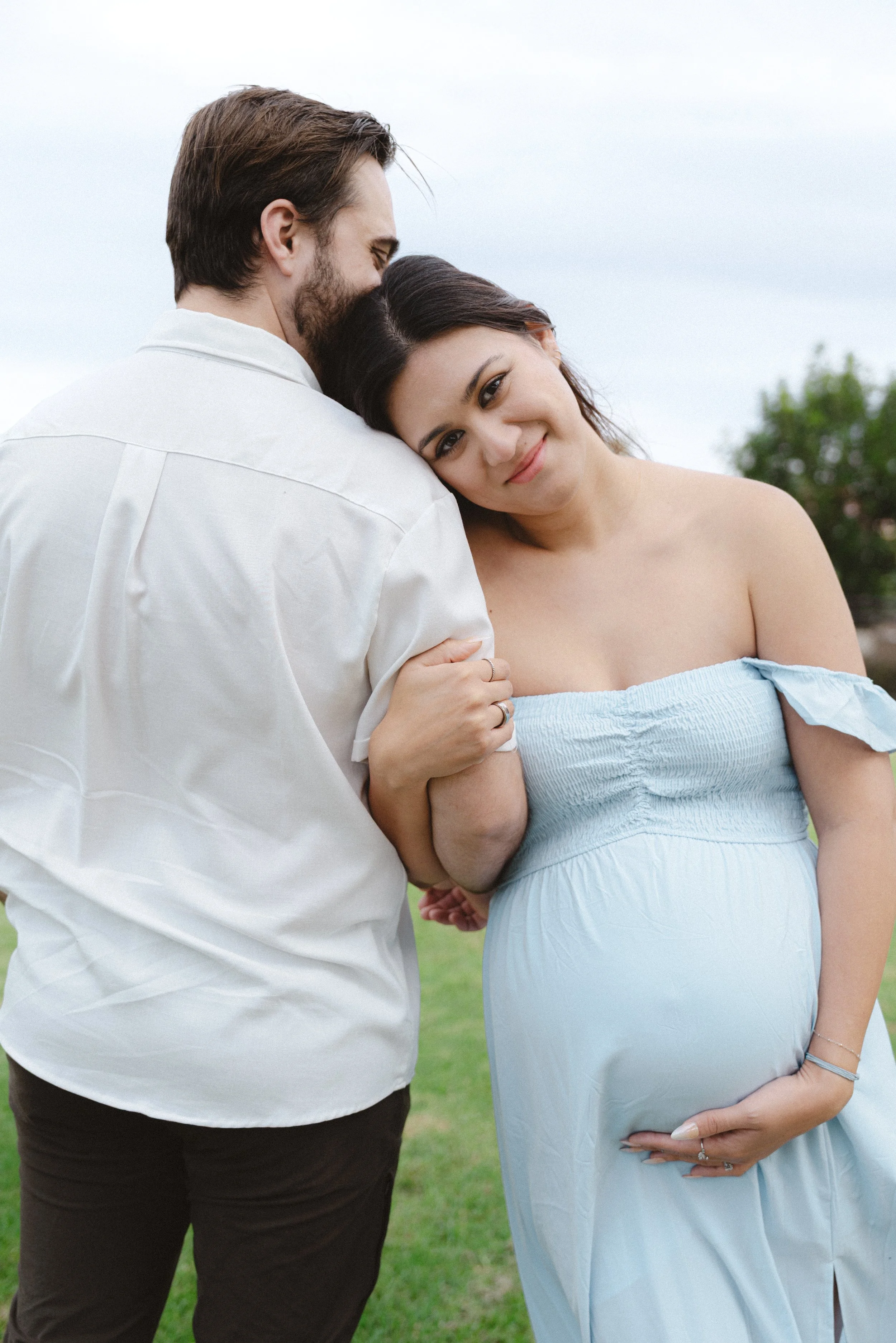 Expecting mother in a light blue dress leaning into her partner during a maternity photoshoot in Dana Point, California.