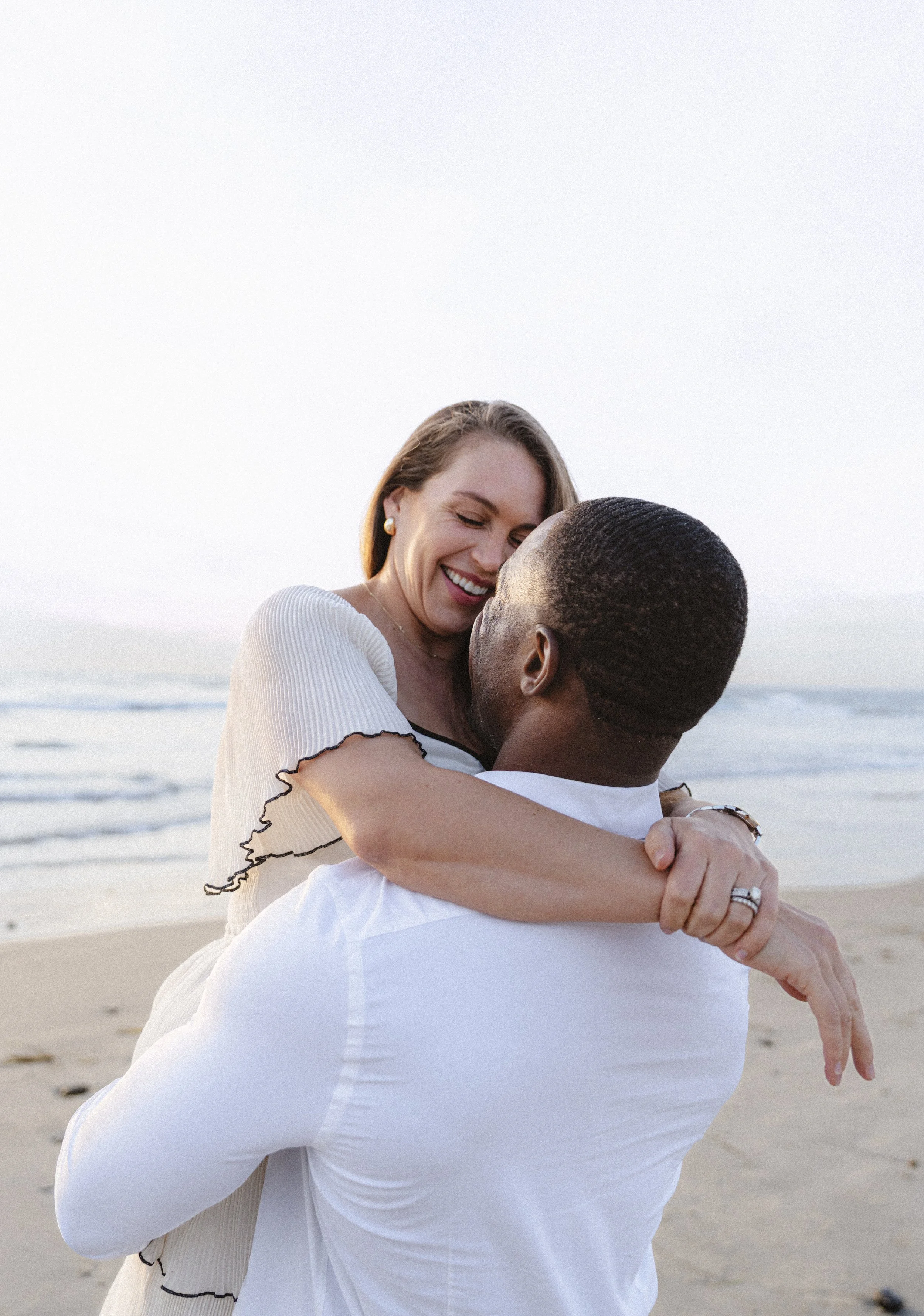 Romantic couple embracing at Ponto Beach in Carlsbad, California during an elegant coastal engagement photo session.