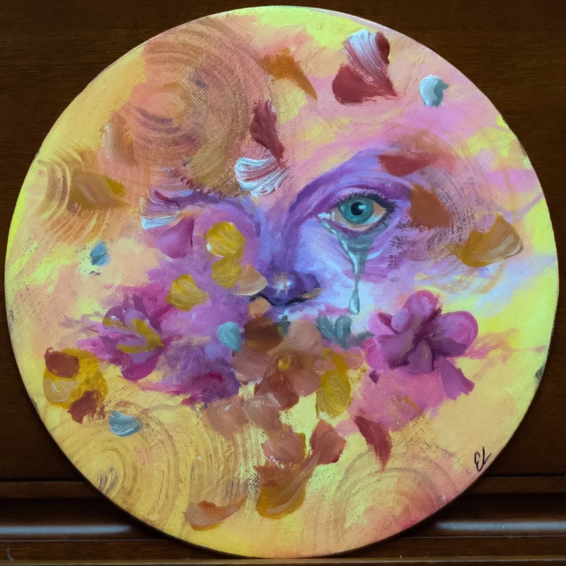 A circular painting of a face with a tear and a blue eye, surrounded by colorful flowers and abstract brushstrokes, blending pastel and vibrant colors.