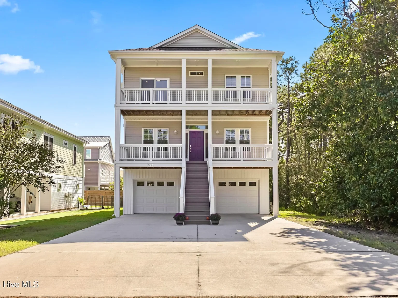 Three-story house with a purple front door, garages on the ground level, and two balconies on upper levels, surrounded by trees and neighboring houses.