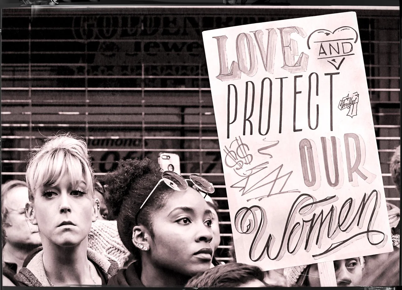 Black and white photo of women protesting, holding a sign that says 'Love and Protect Our Women.'