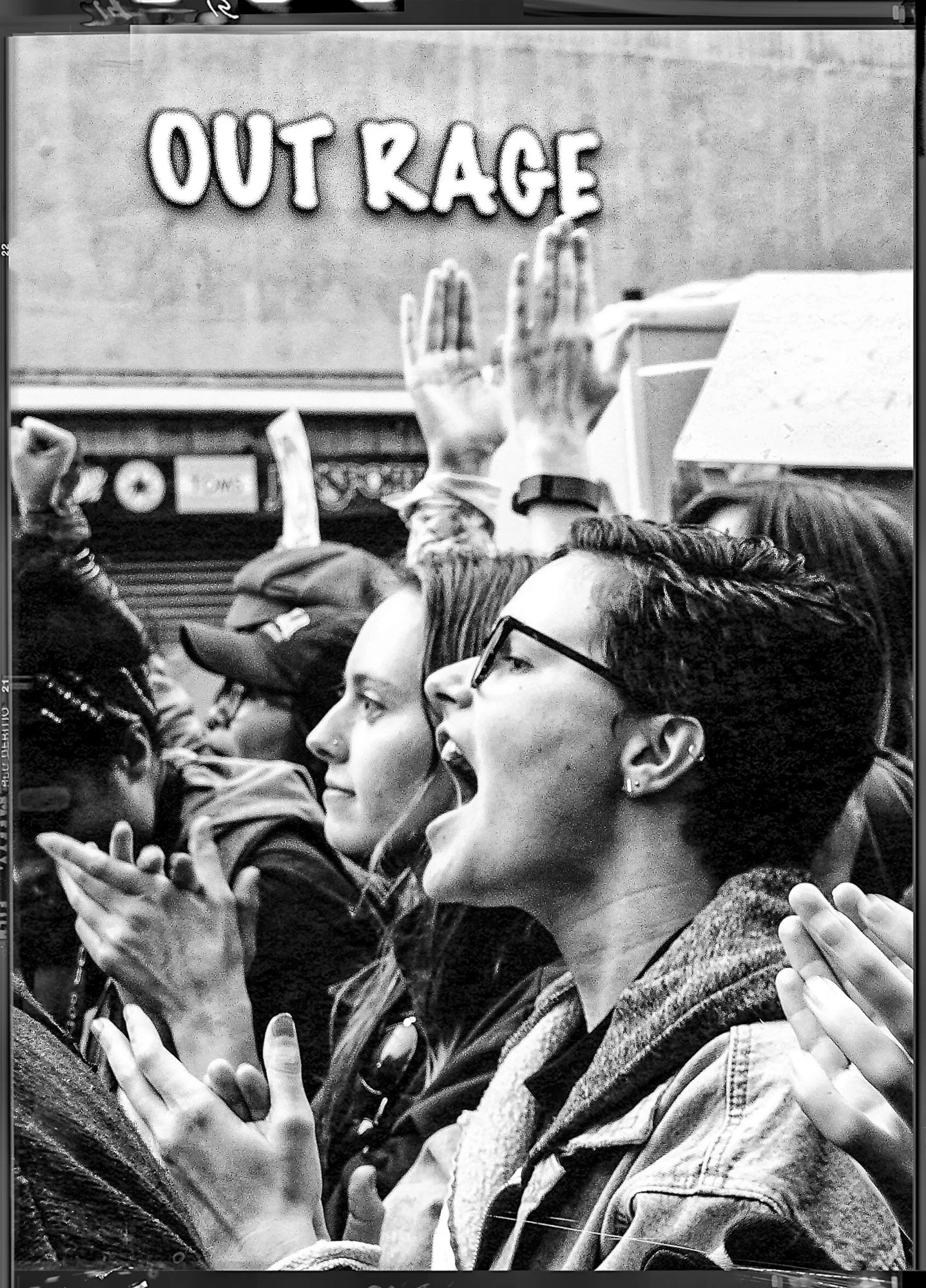 A black-and-white photo of a protest with people holding signs and raising their hands. One woman in the foreground is shouting, and others are clapping and listening attentively. The background has a sign that reads "OUT RAGE."