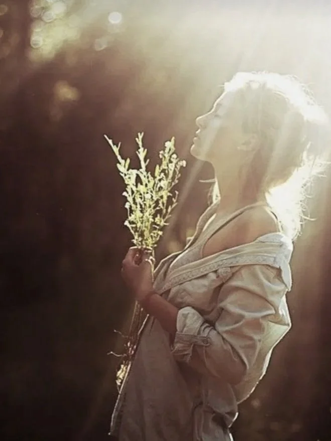 A woman standing in the sunlight holding some flowers.