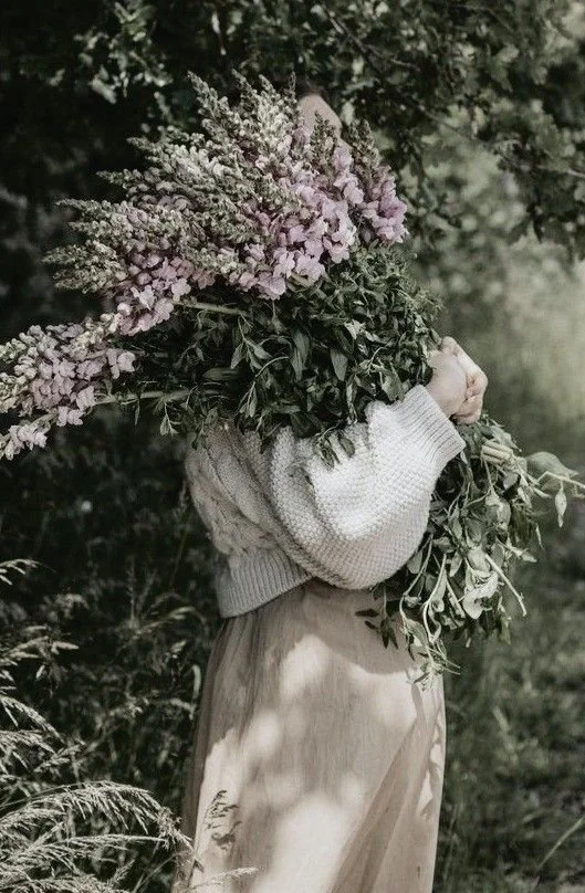 A woman holding a large bouquet of pale purple flowers against dark greenery.