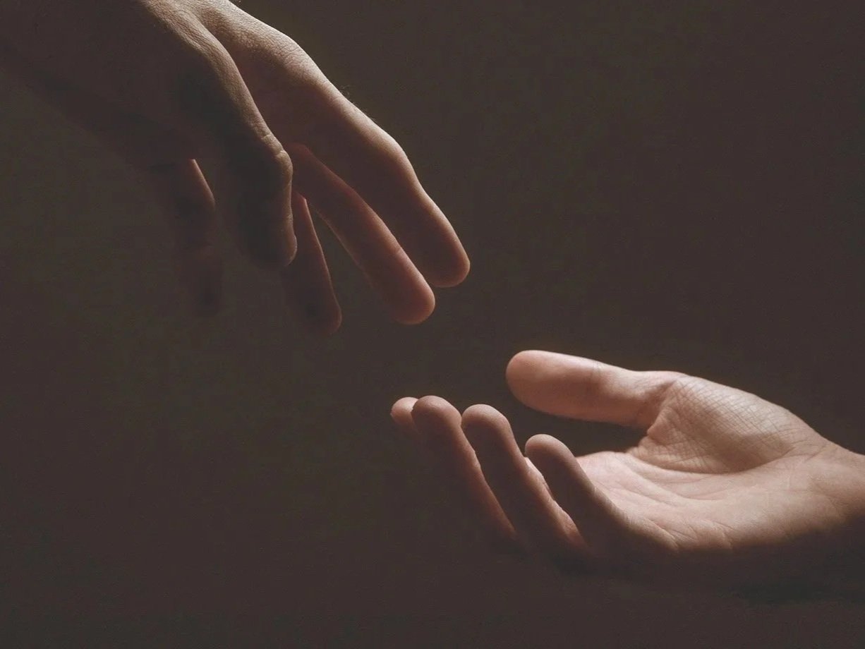 Two hands, one reaching for the other with a darker moody background.
