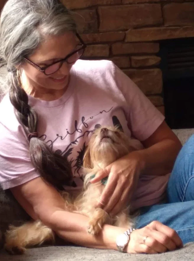A woman sitting down with a small dog beside her looking up at her.