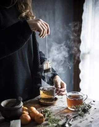 A woman holding a teabag over a cup of water as the steam rises.