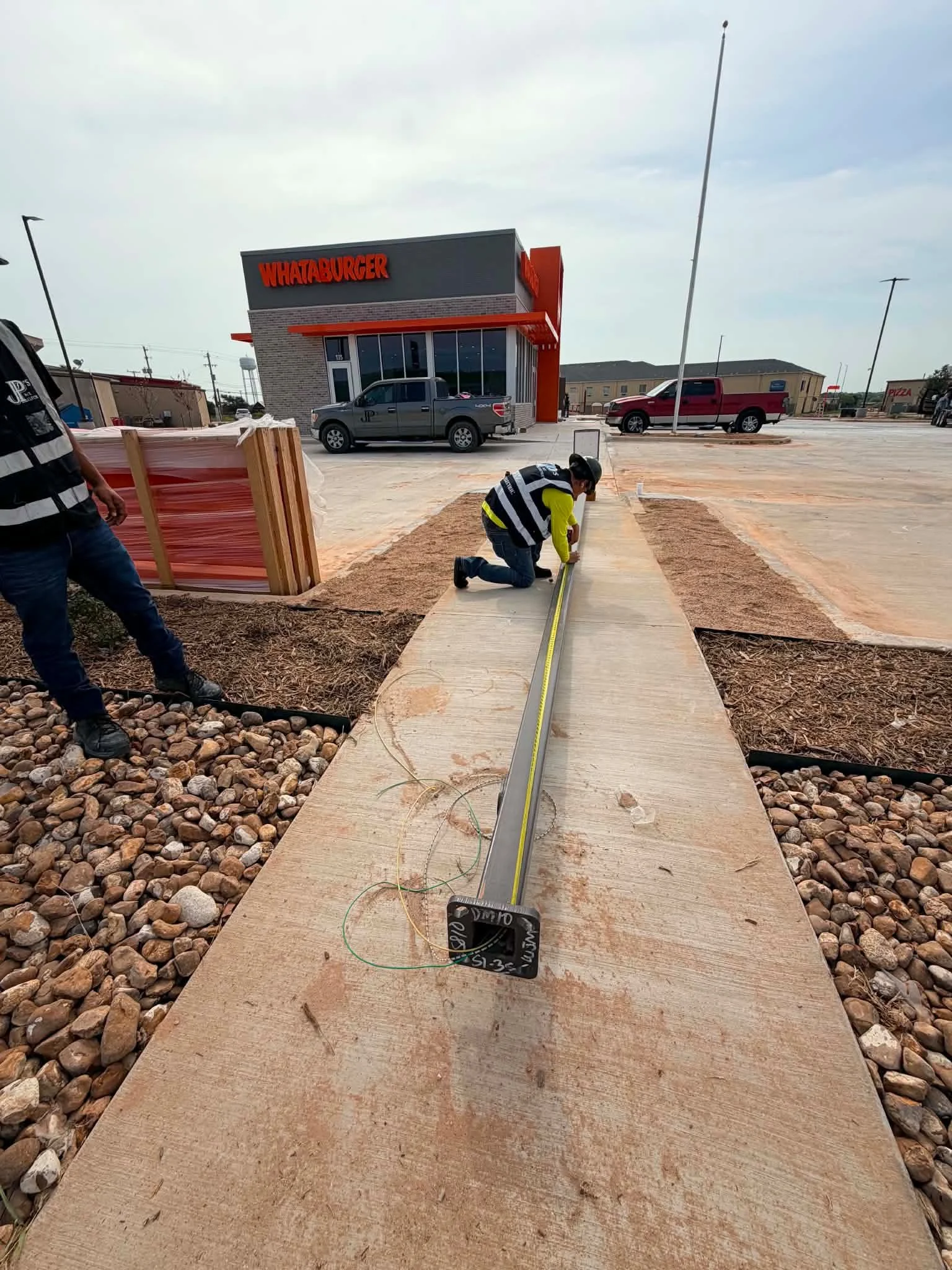 Workers measuring concrete sidewalk at a construction site outside a Whataburger fast-food restaurant.