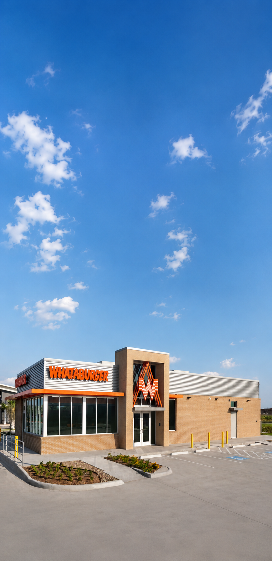 A Whataburger fast food restaurant with a brick exterior, large glass windows, and an orange neon sign in the shape of the letter W against a bright blue sky with scattered clouds.