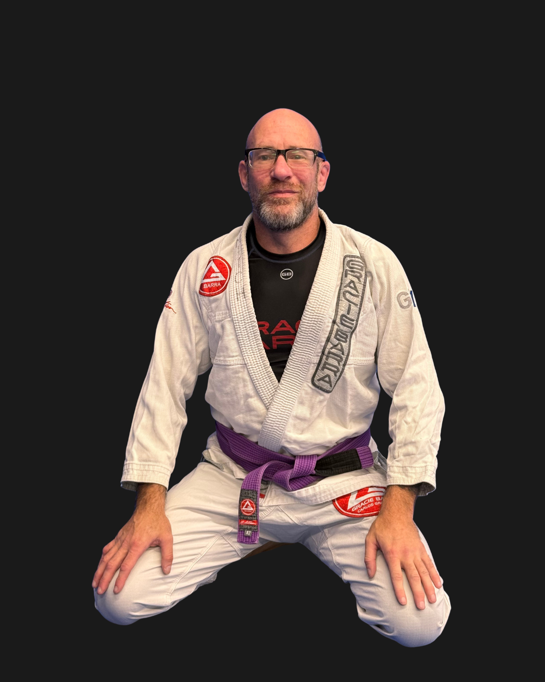 A man in a Brazilian Jiu-Jitsu gi with a purple belt, kneeling on the ground, with a black background and text that says "Coach Mitch GB" in the top left corner.