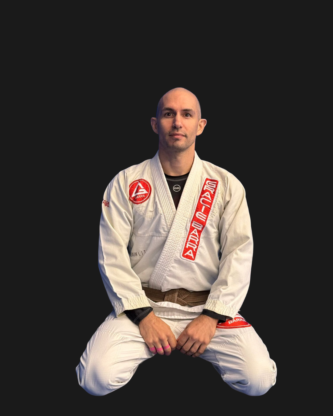 A man kneeling in a Brazilian Jiu-Jitsu gi against a black background.