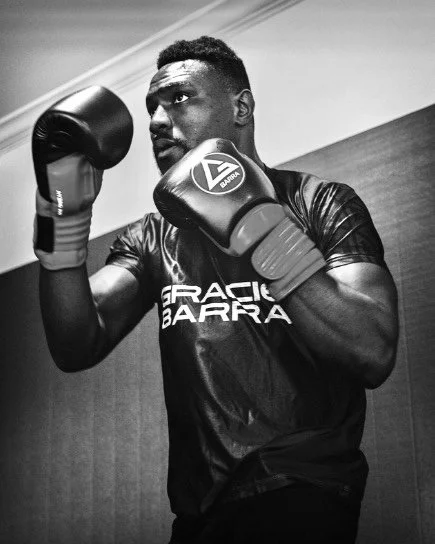 A boxing trainer holding focus mitts for a boxer practicing a kick during training at a gym.