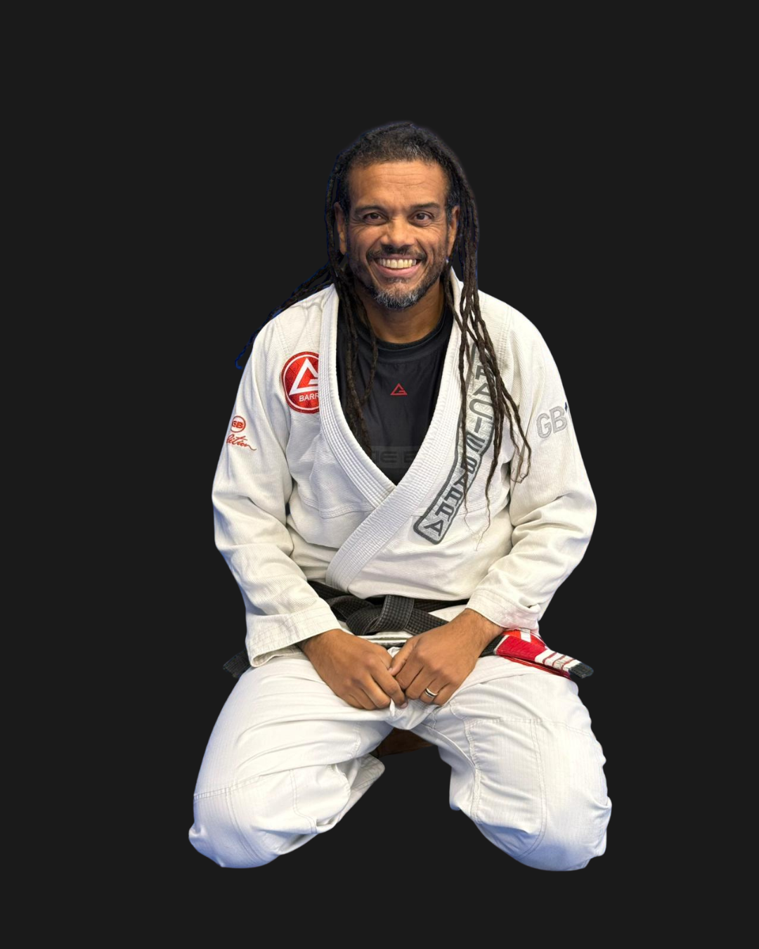 A man with dreadlocks smiling, wearing a Brazilian Jiu-Jitsu gi, kneeling against a black background. The gi has patches and the text 'Professor Brancão' above.