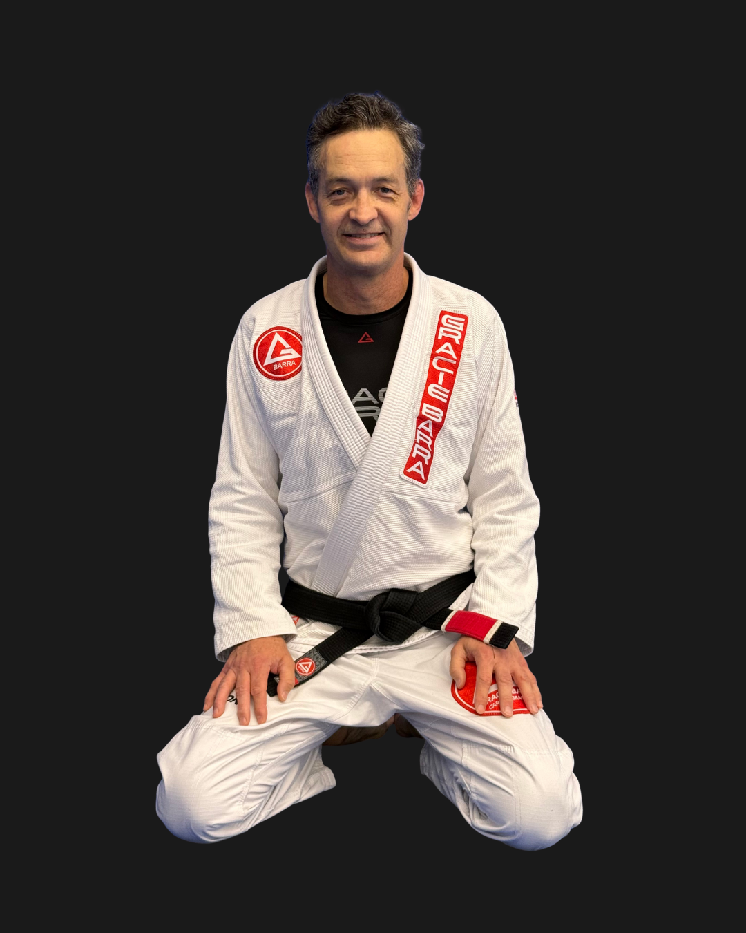 A male Brazilian Jiu-Jitsu practitioner in a white gi with red patches, kneeling on the ground, with text indicating his name and rank in Brazilian Jiu-Jitsu.