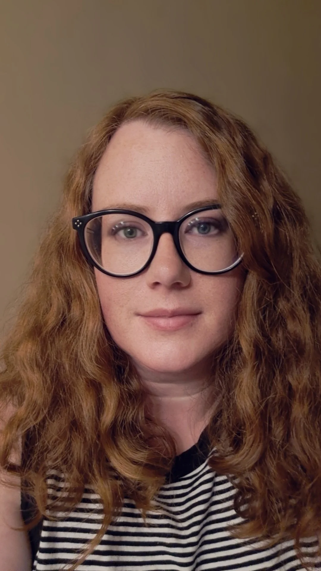Young woman with curly red hair wearing black-rimmed glasses and a black and white striped shirt.