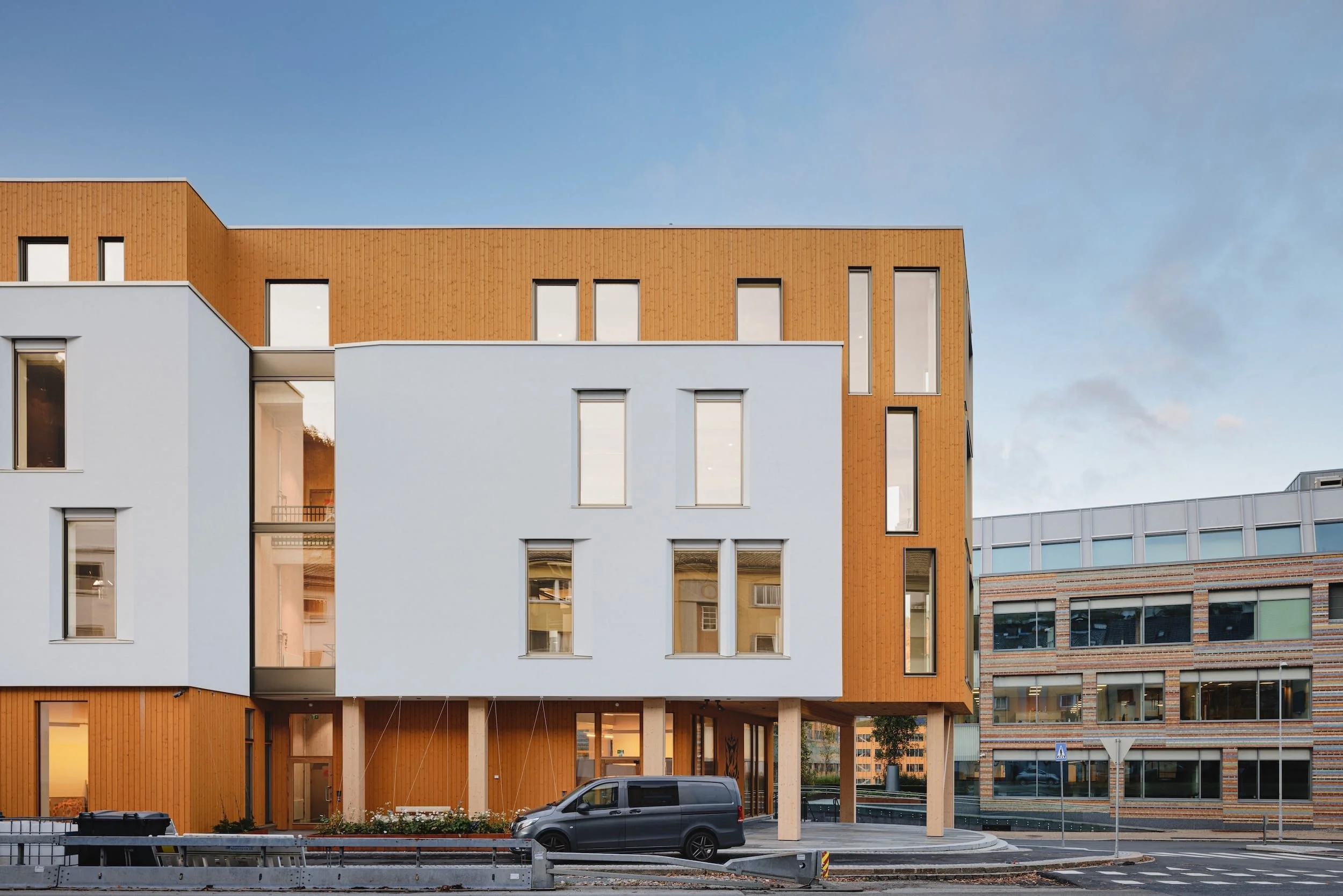Modern multi-story building with white and orange exterior walls, rectangular windows, and a parked van in front. - Damsgård, Bergen