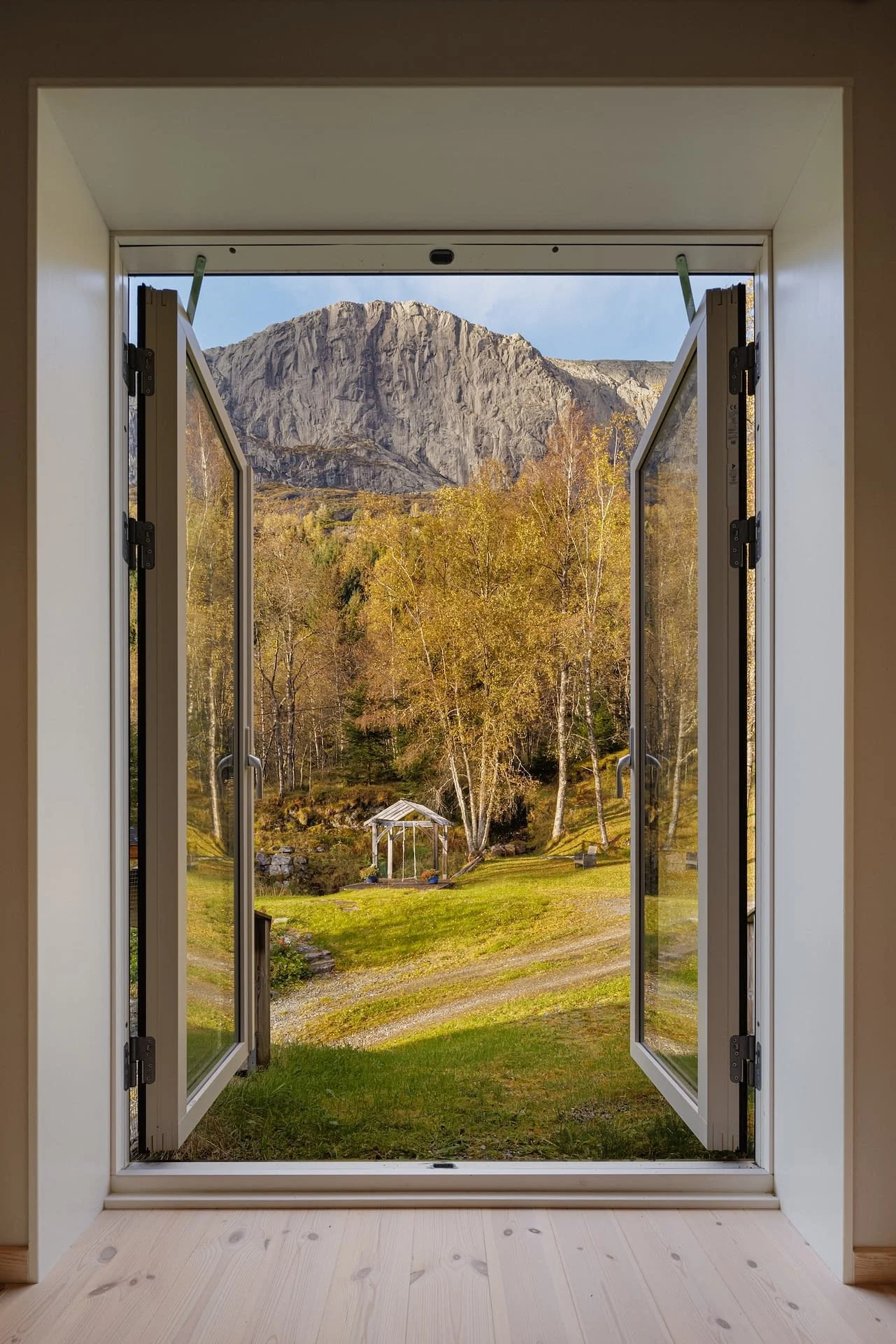 Open door leading to a scenic view of trees, Storehesten mountain, and simple garden. - Bygstad, Sunnfjord