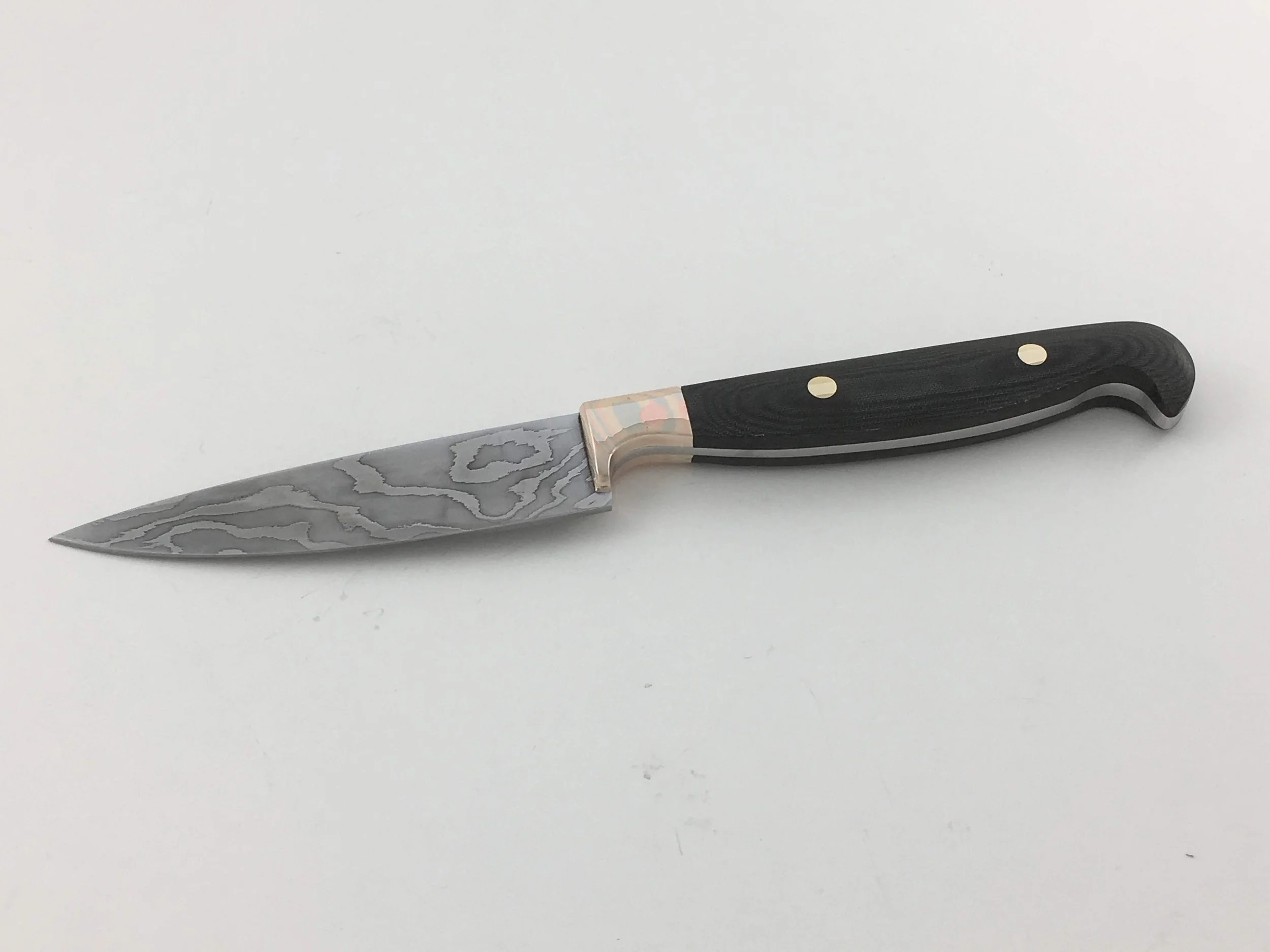 Pairing knife that sold to a family friend. (2018)
Blade: Laminated 5160 and 15N20.
Handle: Full tang construction with black canvas micarta scales and mokume gane bolsters.