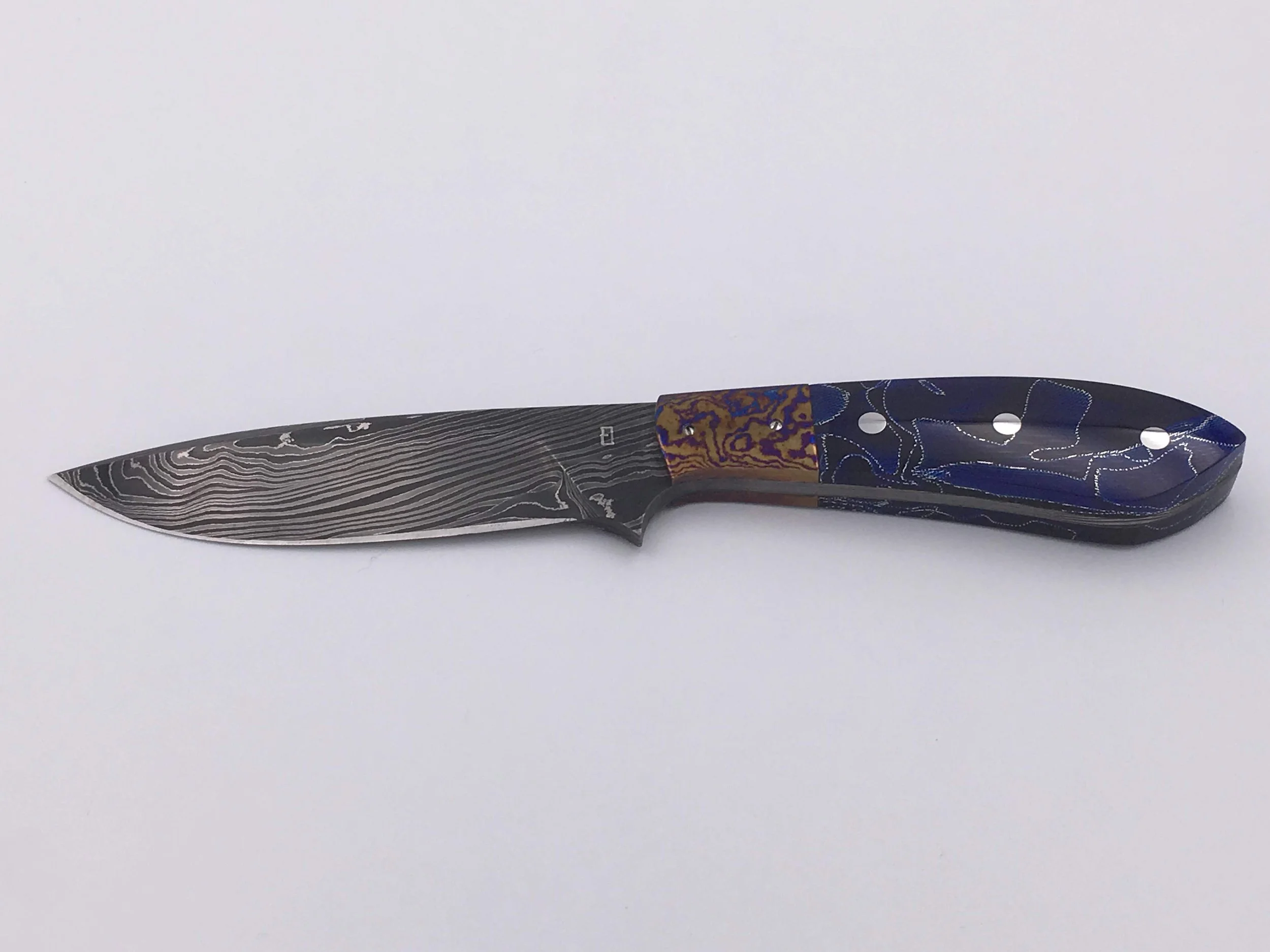 Medium hunting knife I made while learning from Jerry McClure for 2 weeks. (2018)
Blade: Laminated 1095 and 15N20, with pure nickel sheet for contrast.
Handle: Full tang construction with blue Raffir scales and titanium damascus bolsters.