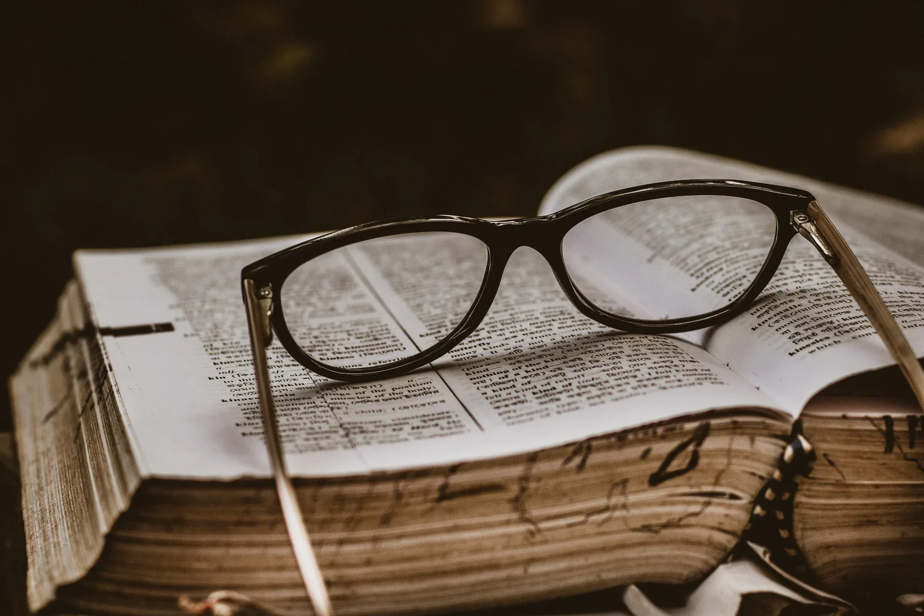 A pair of black eyeglasses resting on an open book with visible text.