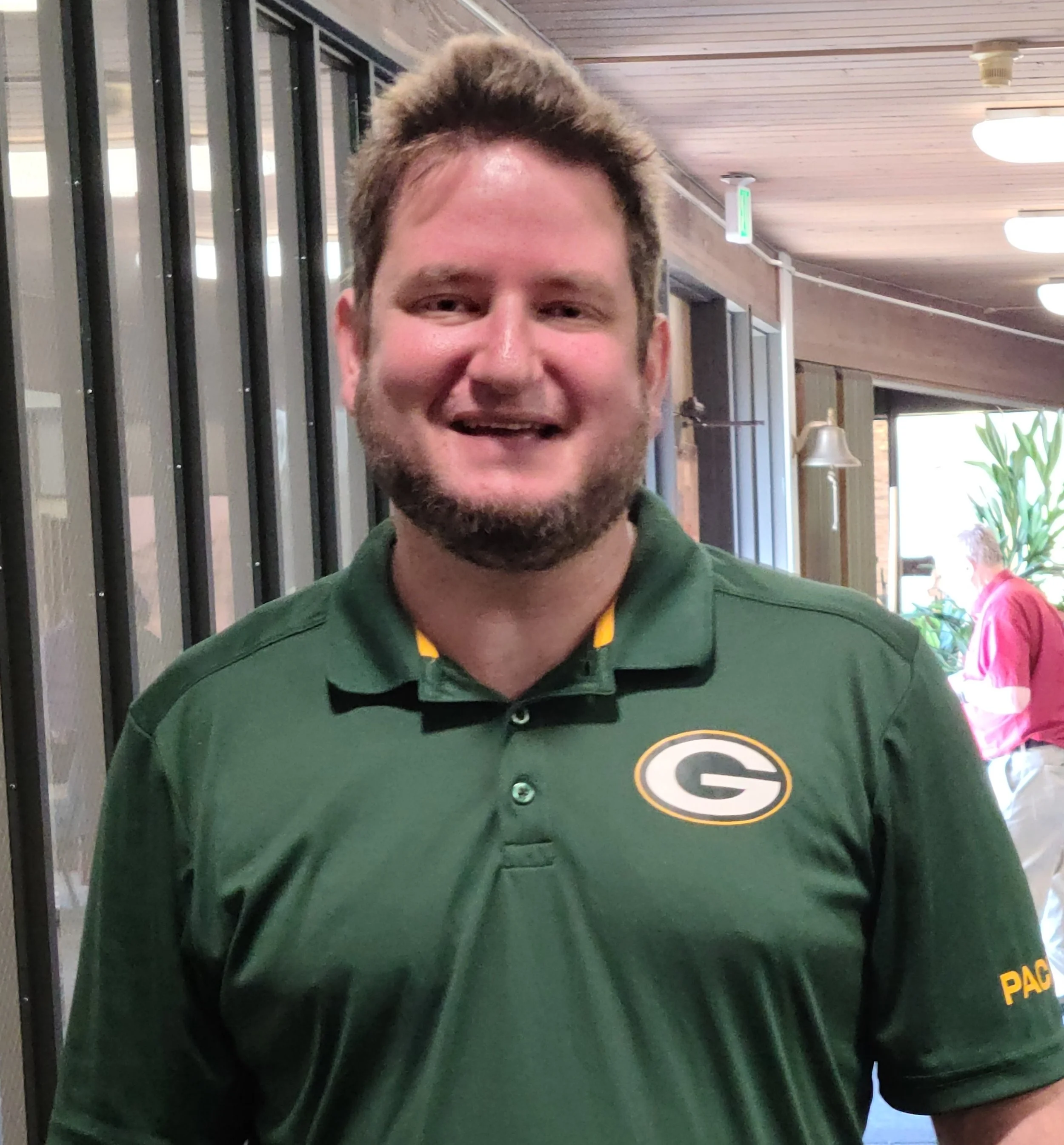 A smiling man wearing a green Green Bay Packers polo shirt.