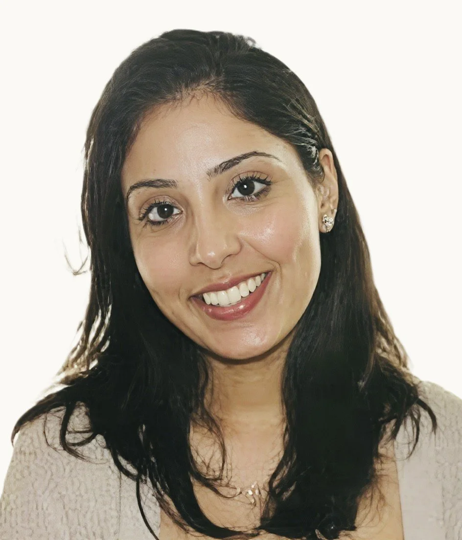 Close-up of a smiling woman with dark hair, wearing earrings and a light-colored top against a plain background.