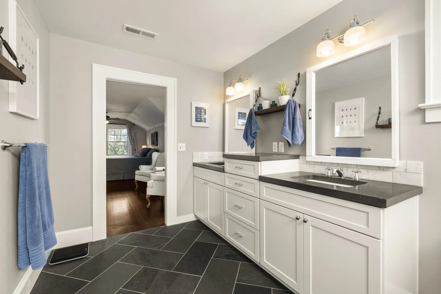 Bathroom with white cabinets, black countertops, and blue towels, connected to a bedroom through an open door.