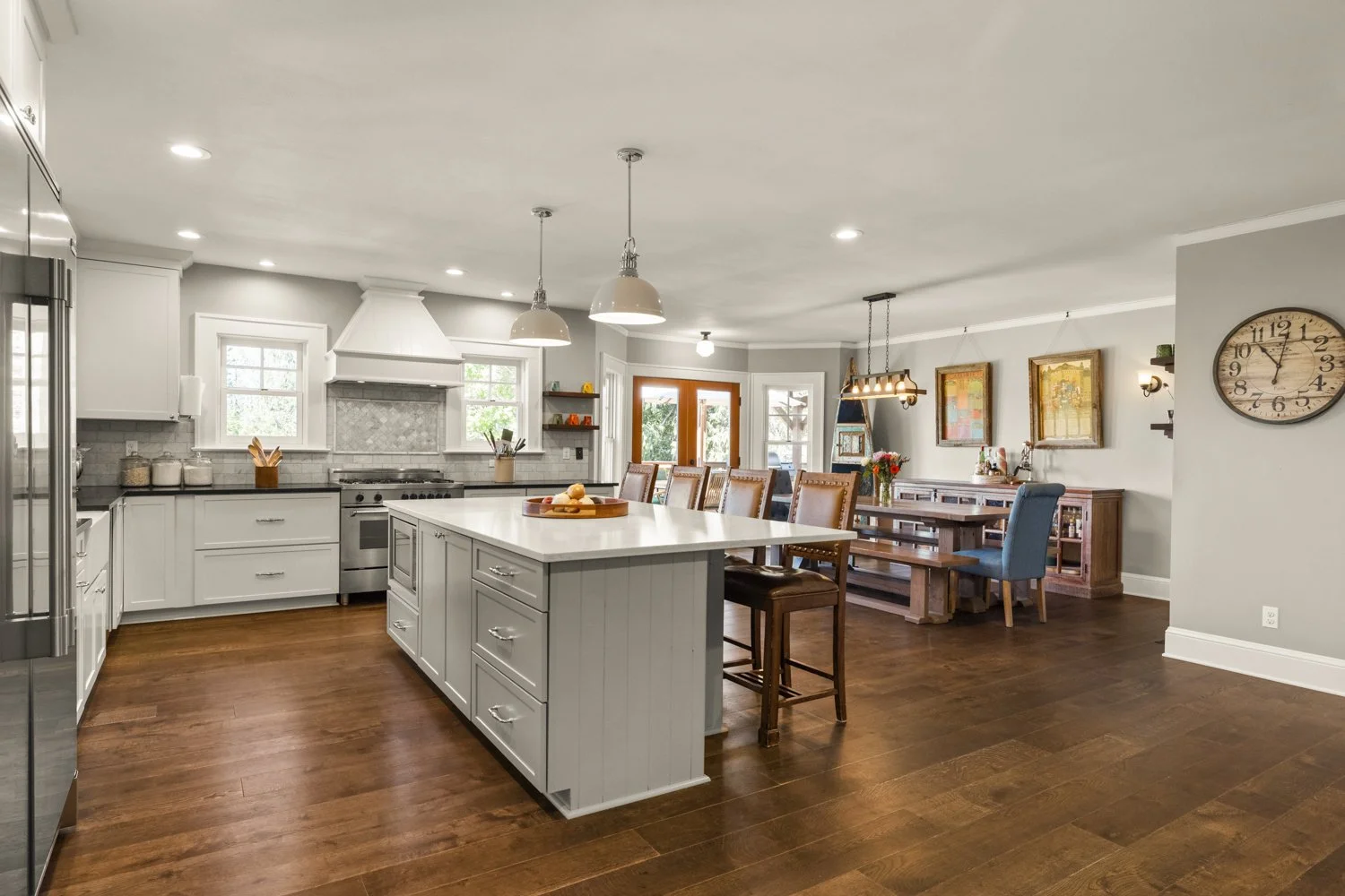 Bright, spacious kitchen with white cabinets, island with white countertop, stainless steel appliances, and a dining area with a wooden table and colorful chairs.