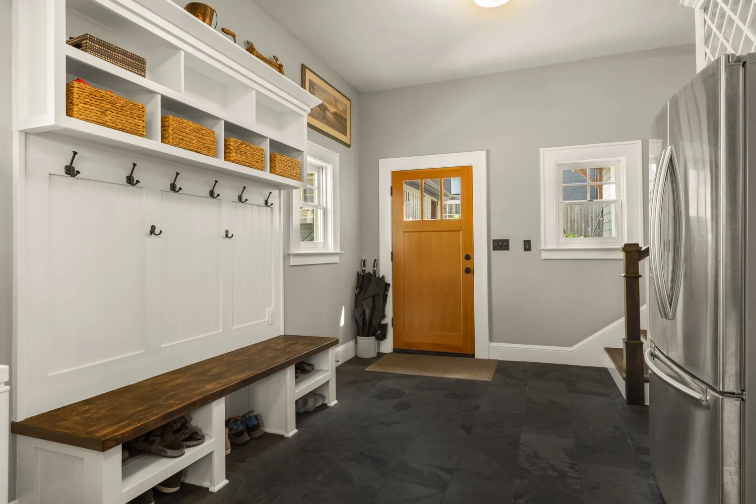 Entryway with a wooden door, gray walls, black slate floor, and white built-in storage with hooks, shelves, and shoe cubbies.