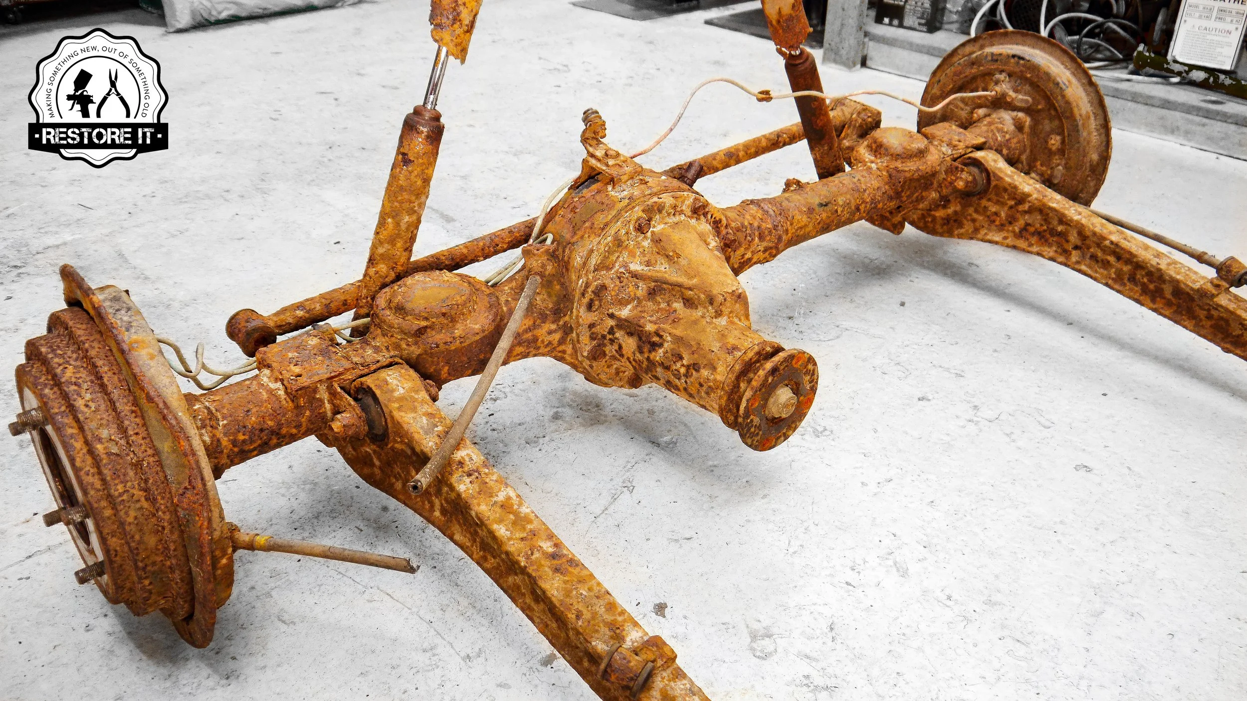 Old, rusted car differential and axle assembly on a concrete floor.