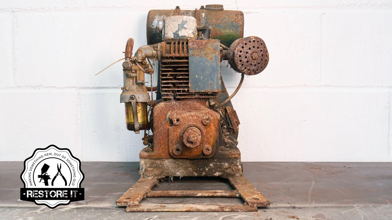 Old, rusted vintage engine on wooden surface against a white wall.