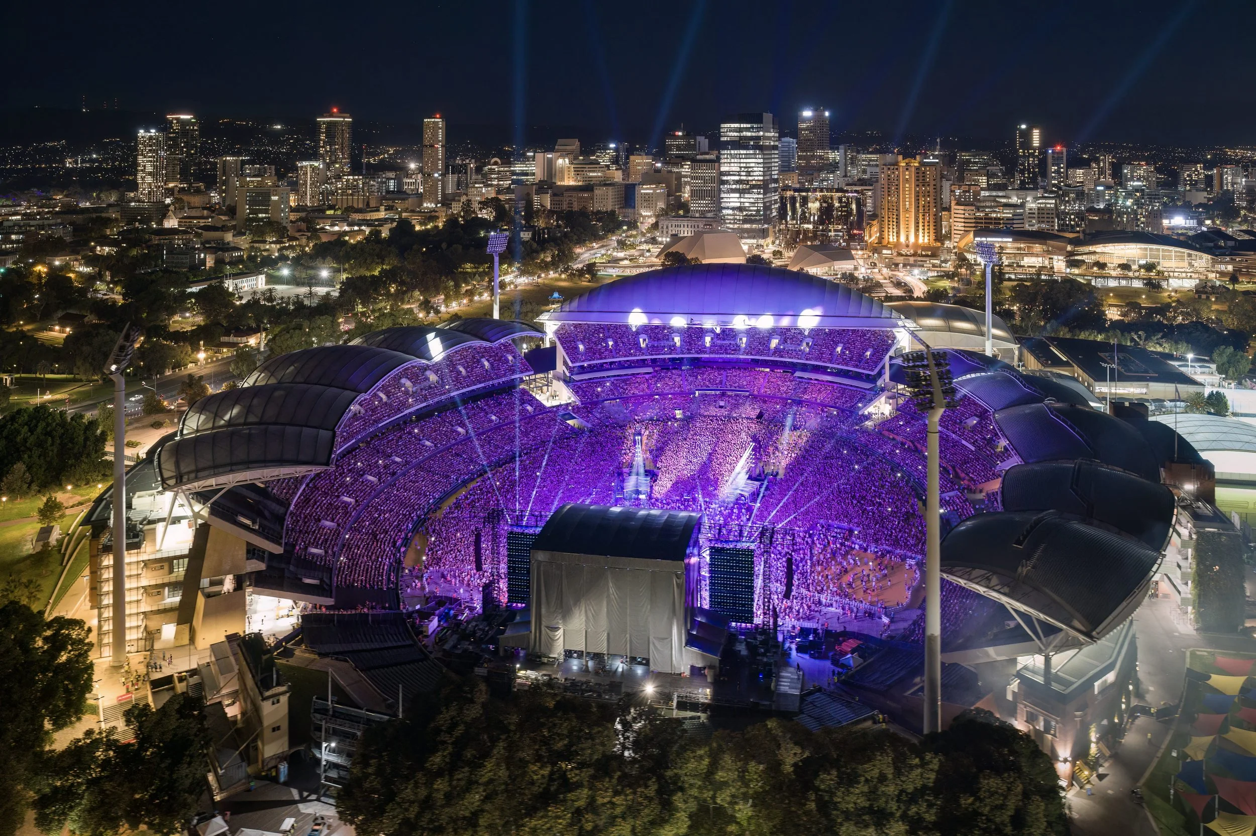 Photo of Adelaide Oval and Adelaide CBD from above at night time. The stadium is lit up in a purple colour. Image Credit: South Australian Tourism Commission.