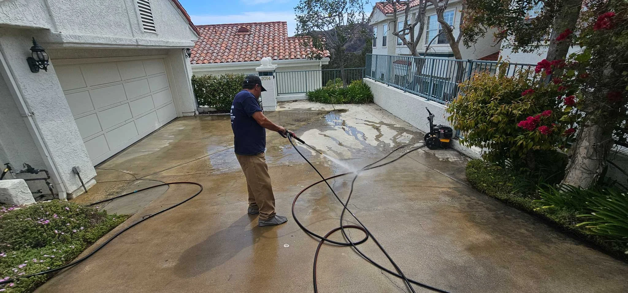 A man washing a concrete driveway with a power washer, wetting the surface.
