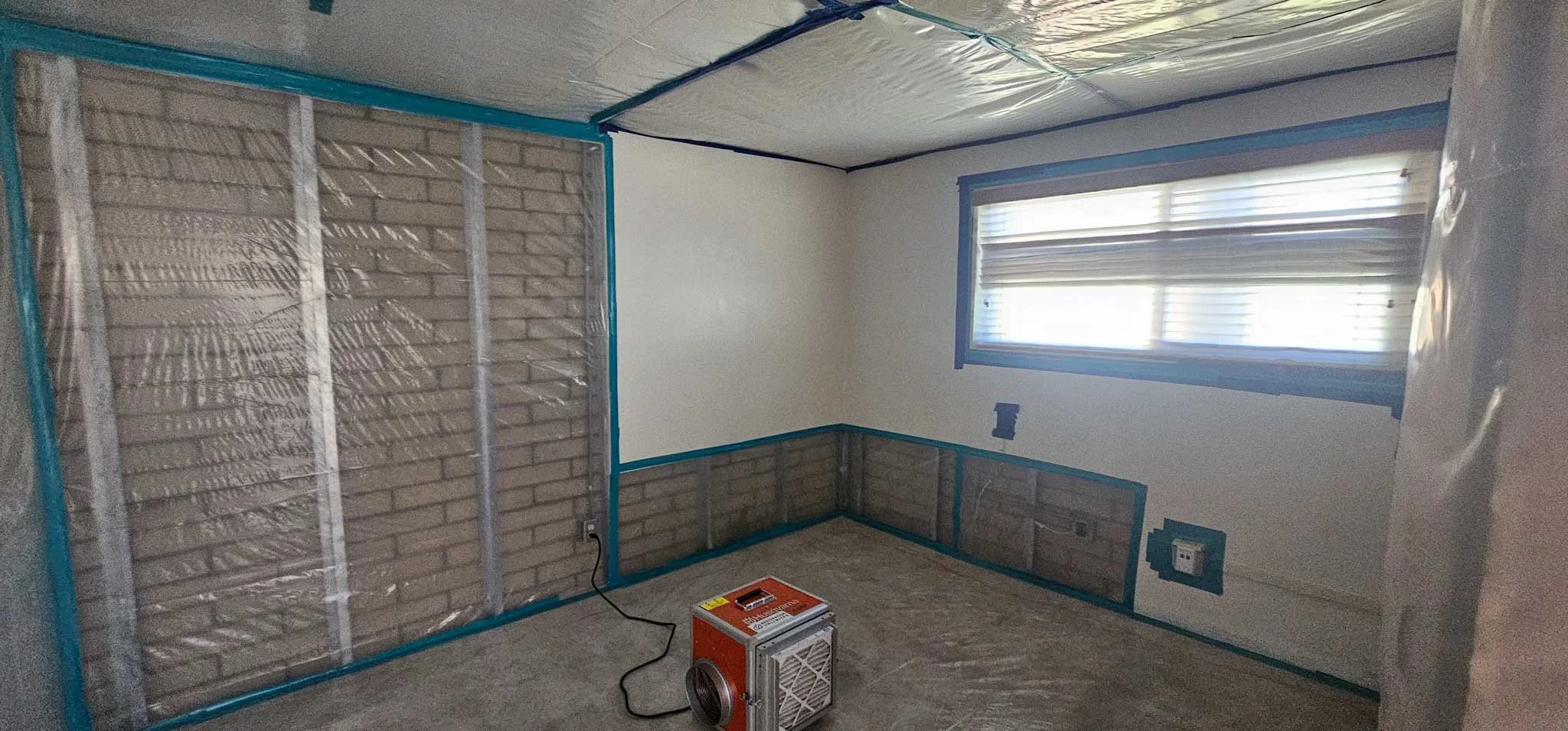 Room under renovation with partially finished walls, plastic-covered ceiling, blue painter's tape, and a small portable heater on the floor.