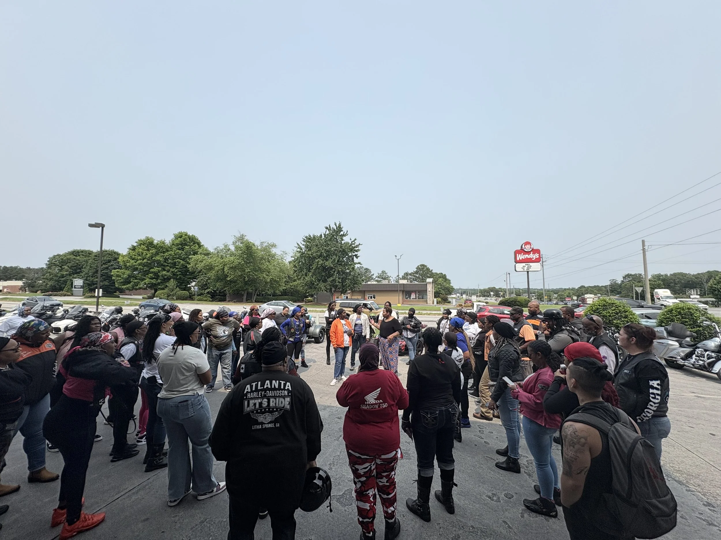 Group of people gathered outdoors near a Wendy's fast-food restaurant, standing in a circle on parking lot pavement.