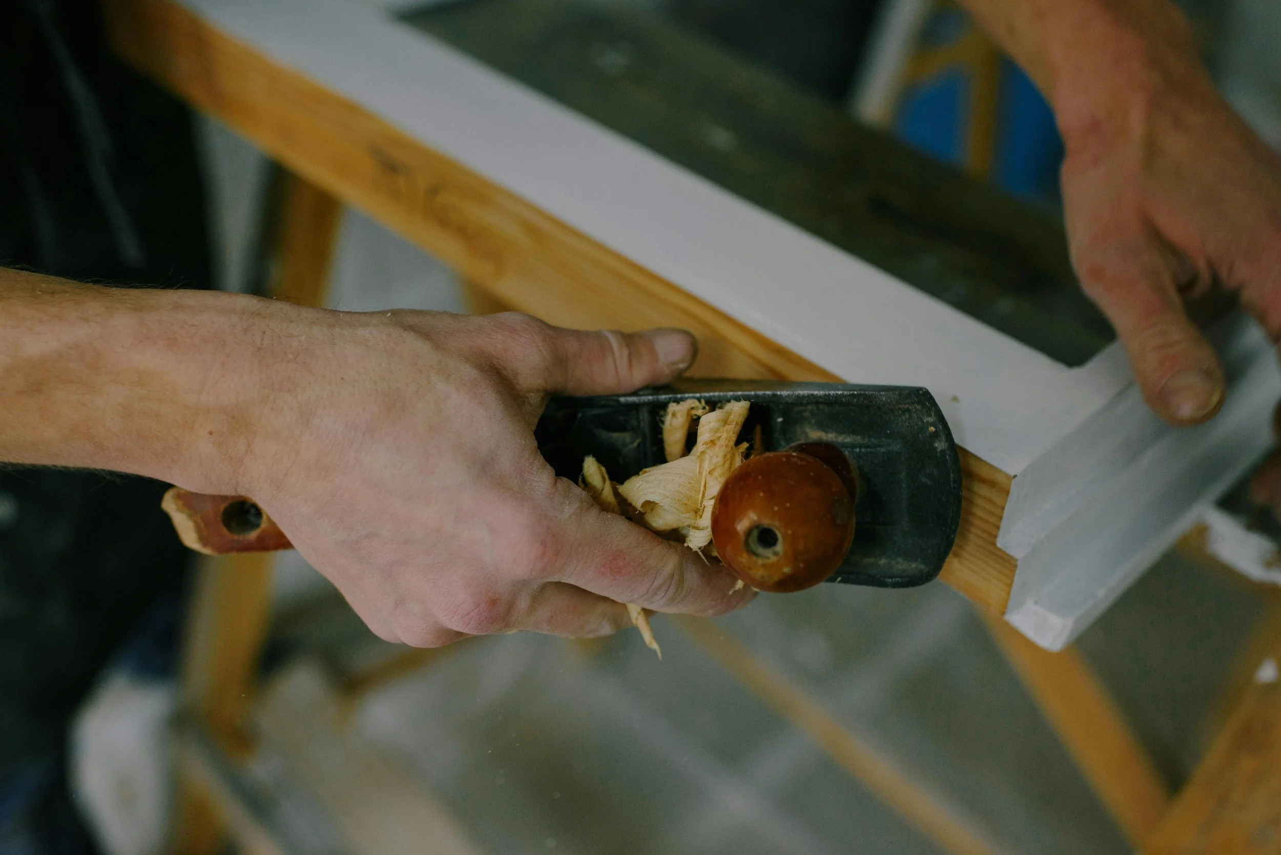 Person using a hand planer to smooth a wooden surface in a woodworking workshop.