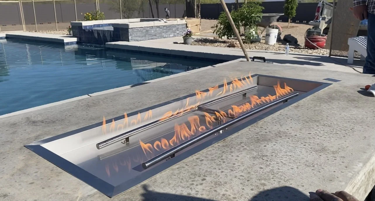 Outdoor pool with a fire feature in front, featuring a rectangular fire pit with flames.