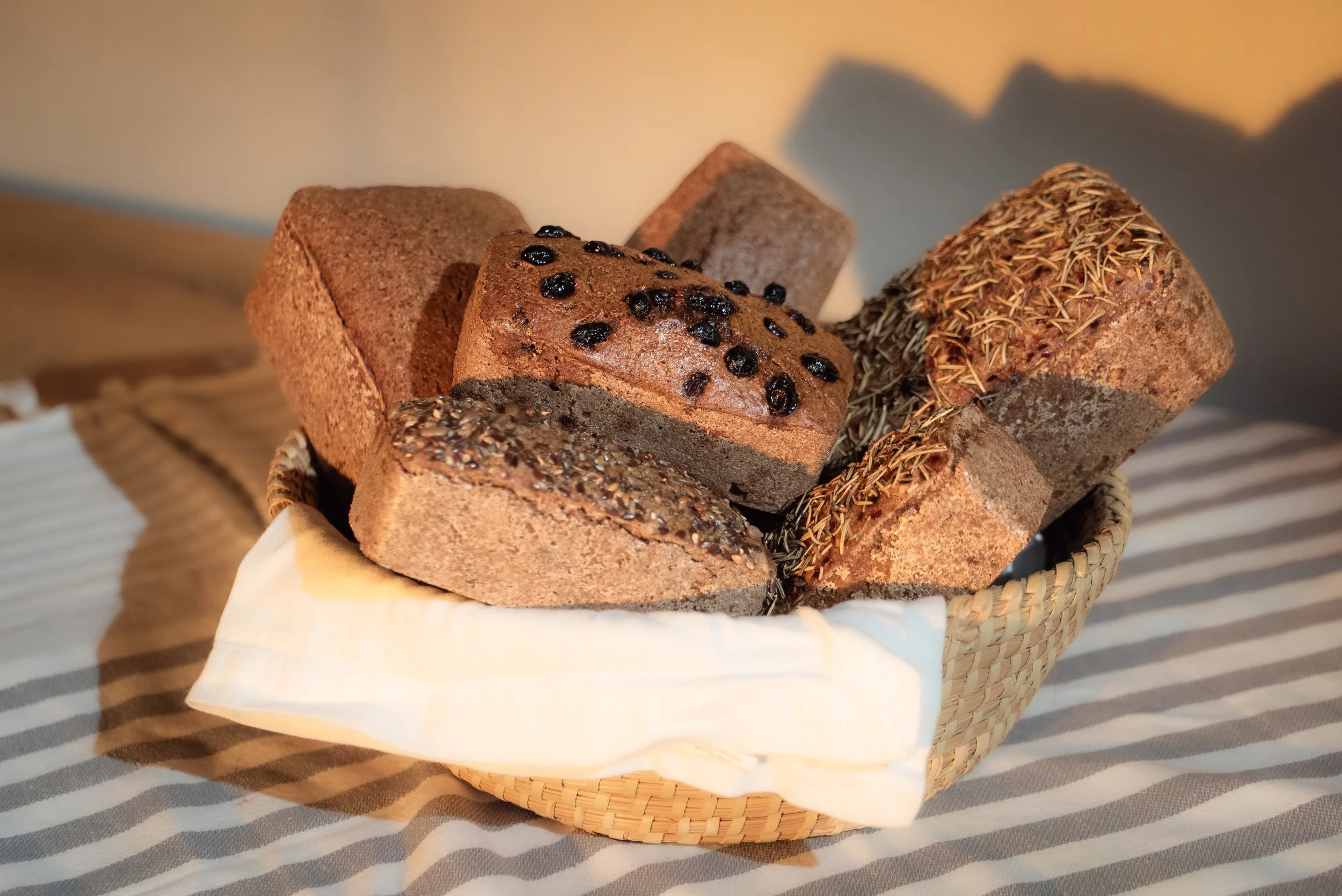 Basket filled with assorted slices of whole grain and multigrain bread on a striped cloth background.