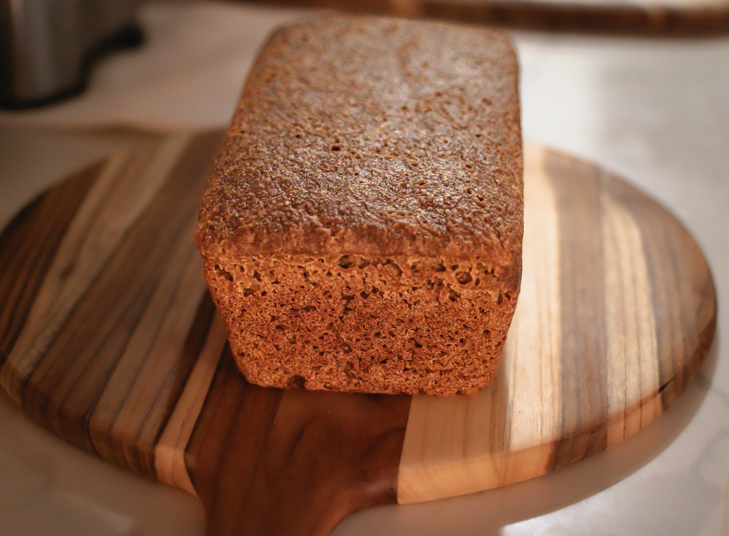 A  Classic Loaf of sourdough bread with organic gluten-free ingredients on a round wooden cutting board.