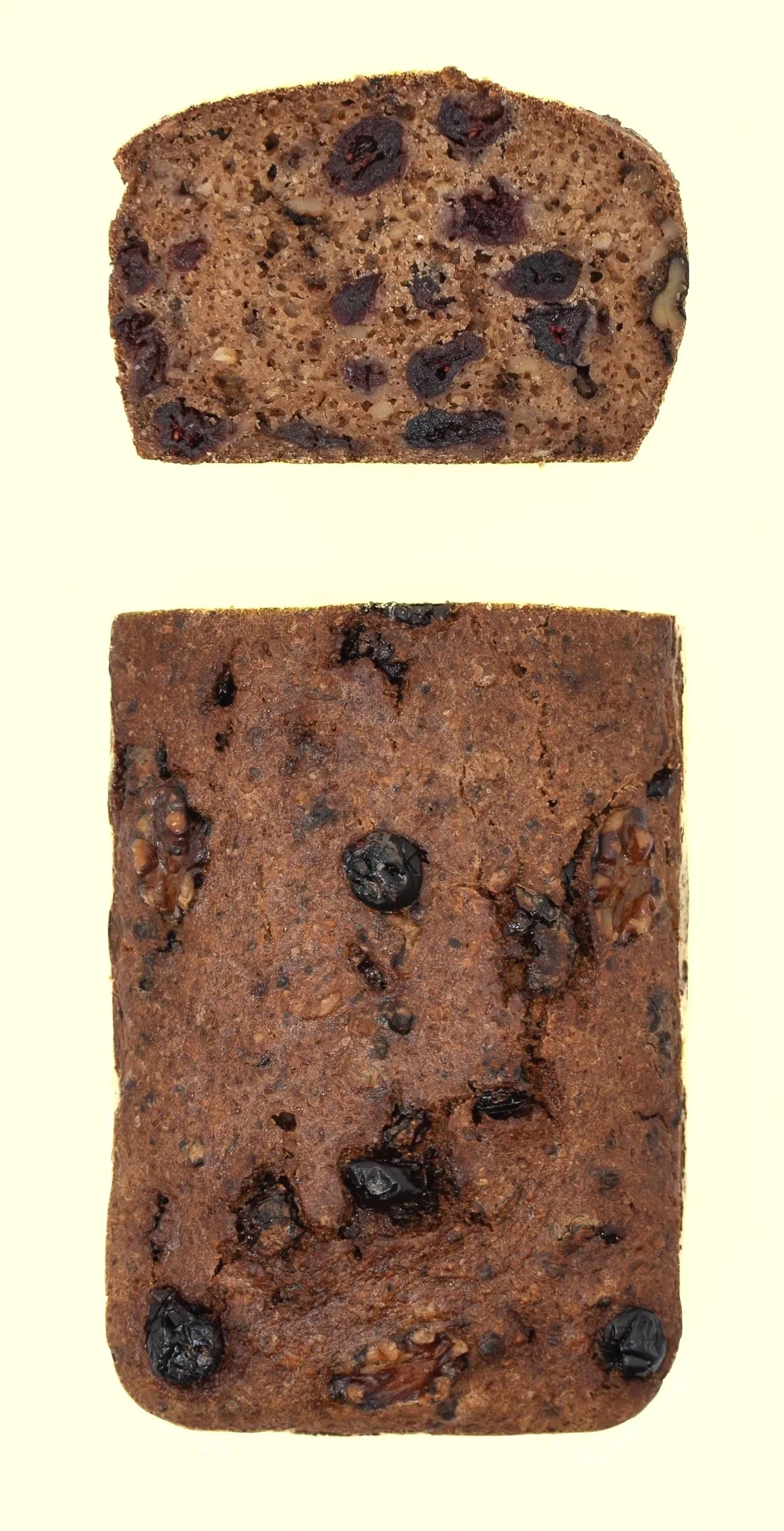 Two pieces of fruitcake with dried fruits and nuts, one sliced and one whole, on a plain light background.