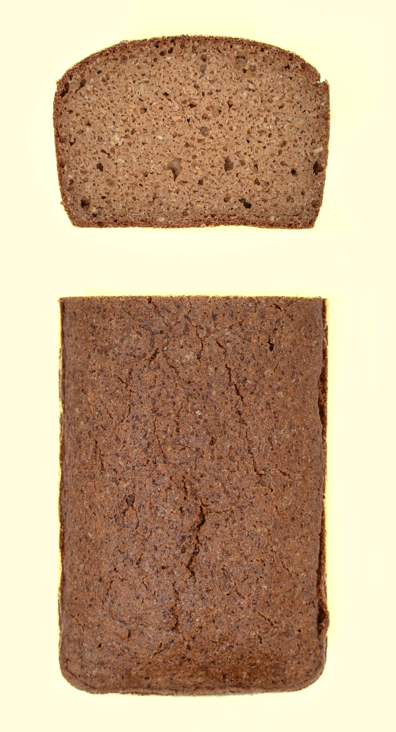 A close-up image of two slices of brown bread, one on top of the other, on a light yellow background.