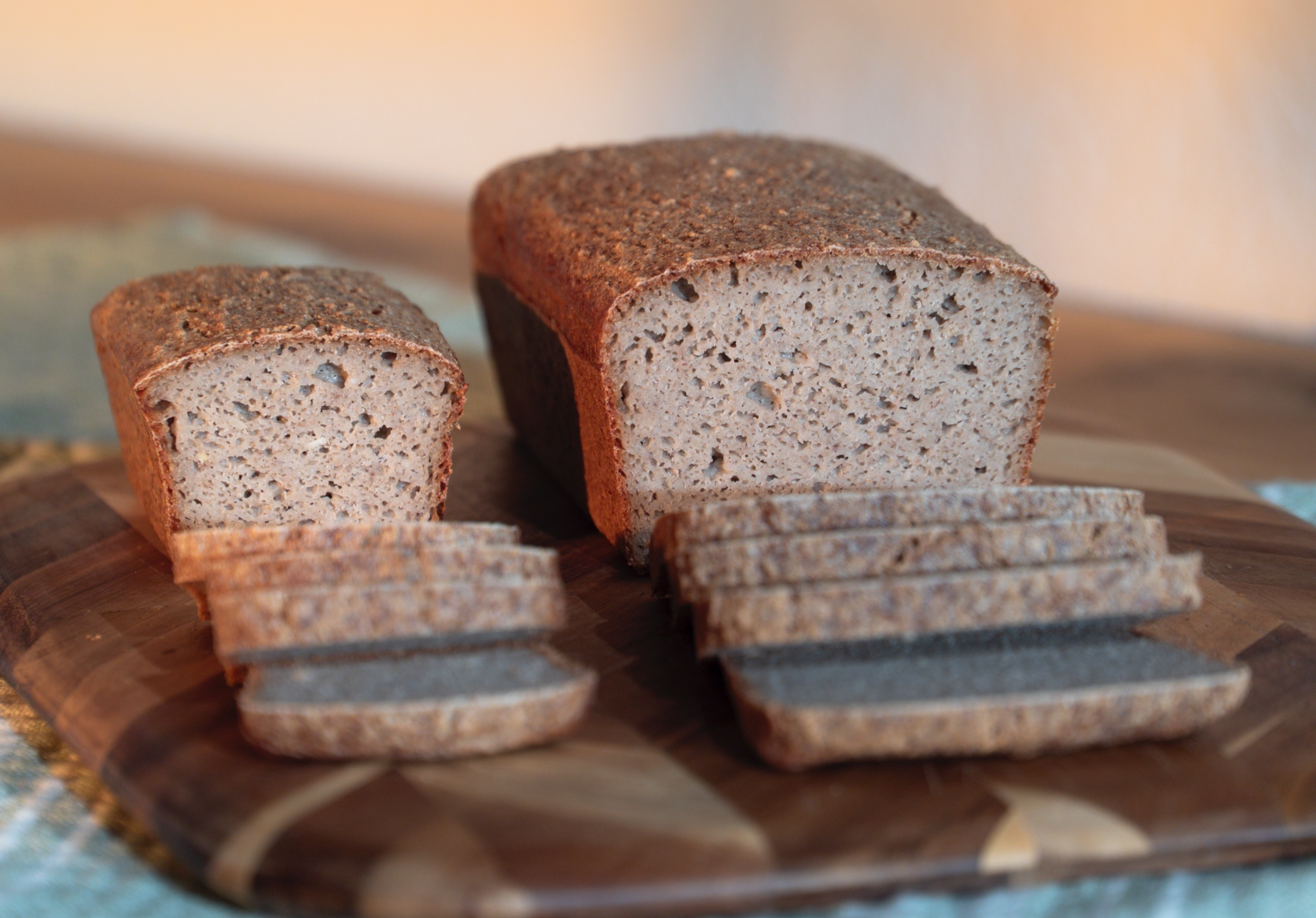 Classic Loaf and classic mini loaf of sliced Sourdough bread made with organic gluten-free ingredients on a wooden cutting board.