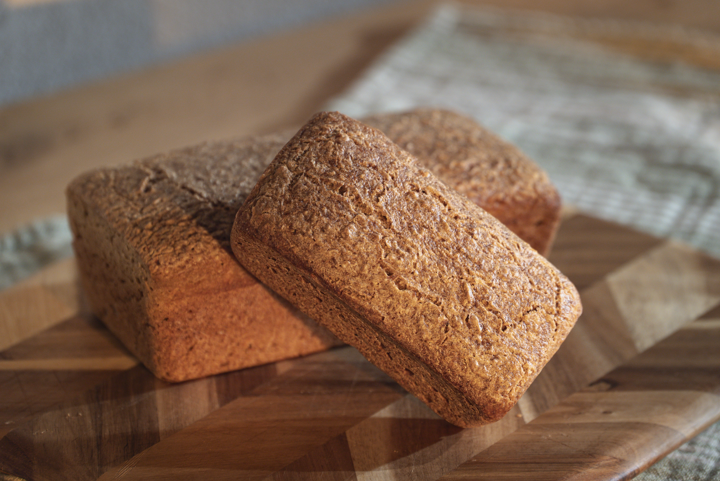 Three rectangular loaves of Sourdough Bread made with organic gluten-free ingredients on a wooden cutting board.