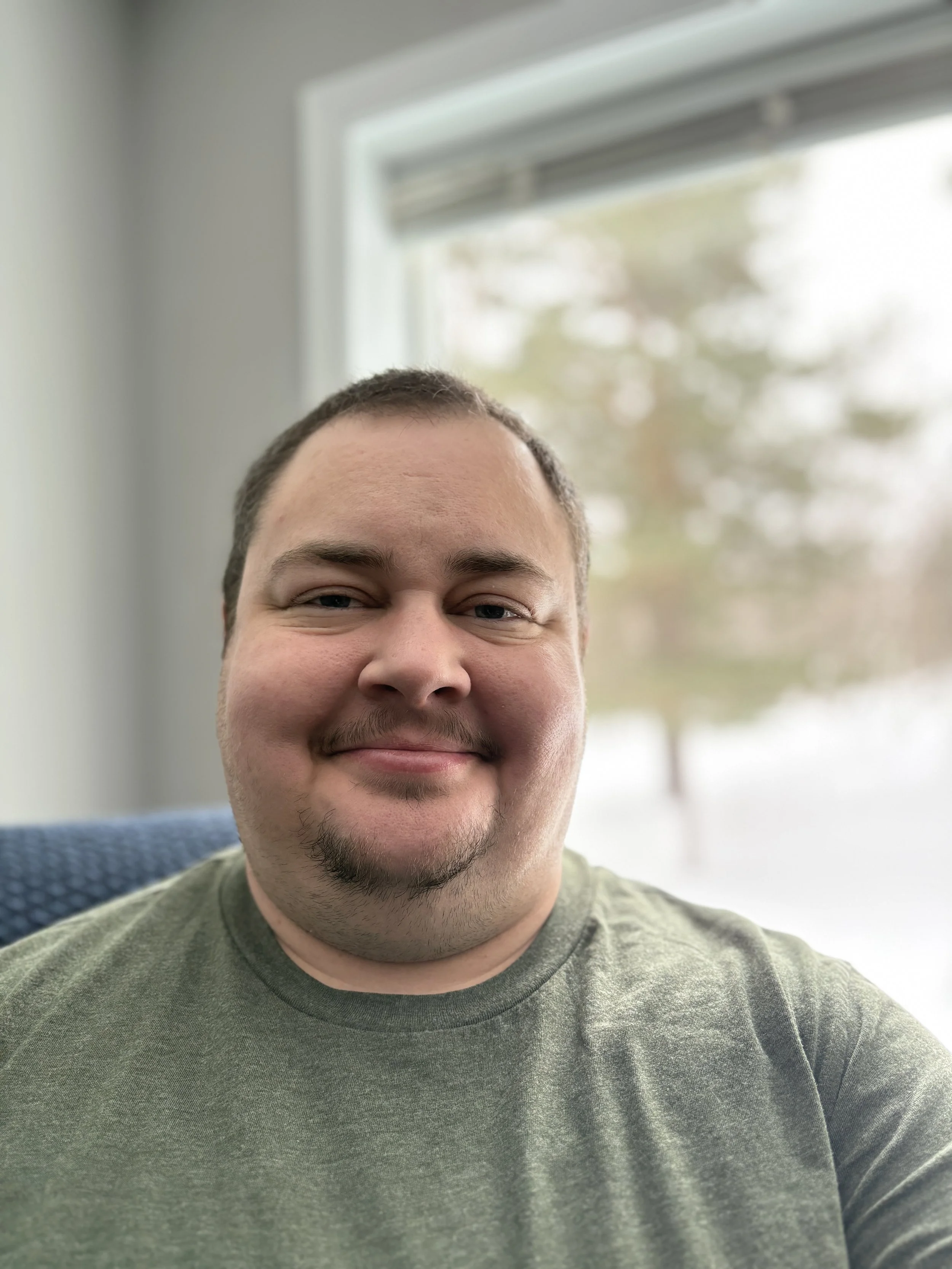 Photo of Root a light skinned person with short brown hair  and beard stubble with a green shirt