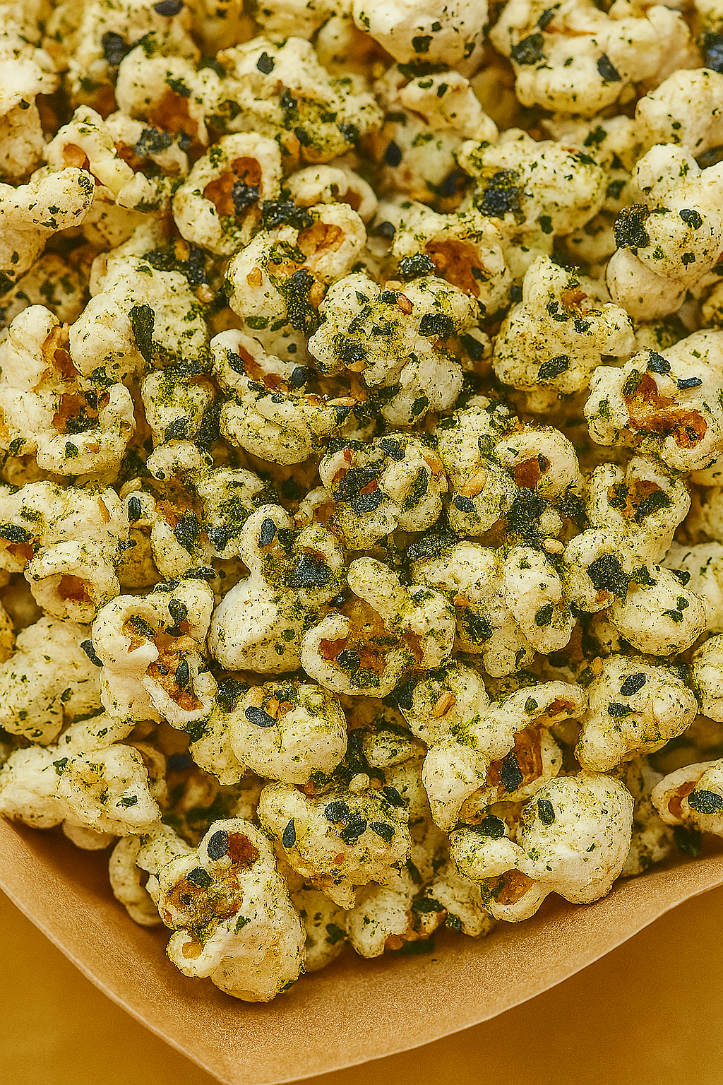 Close-up of spicy popcorn with green and black seasoning in a paper container.