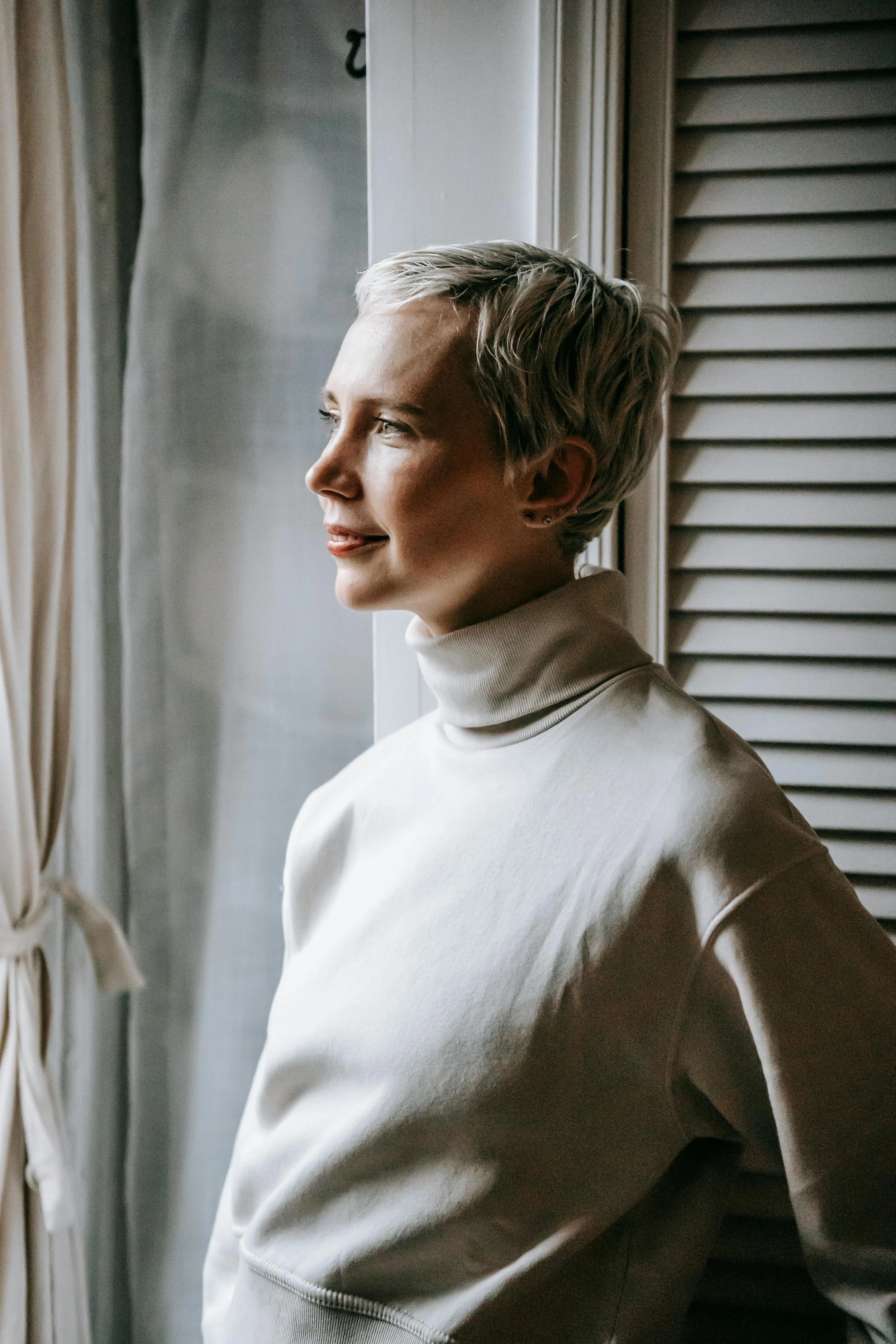 Professional woman gazing out a window in a reflective moment, representing trauma therapy for high-functioning adults